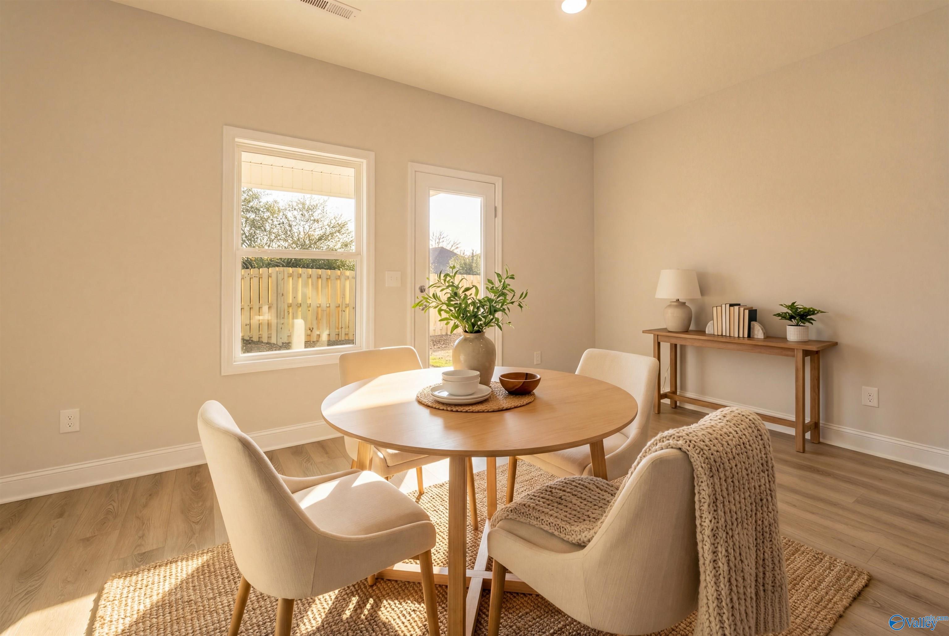 Bright dining room with round wooden table, cream chairs, potted plants, and deck view through large windows in The Camden, Huntsville, Alabama