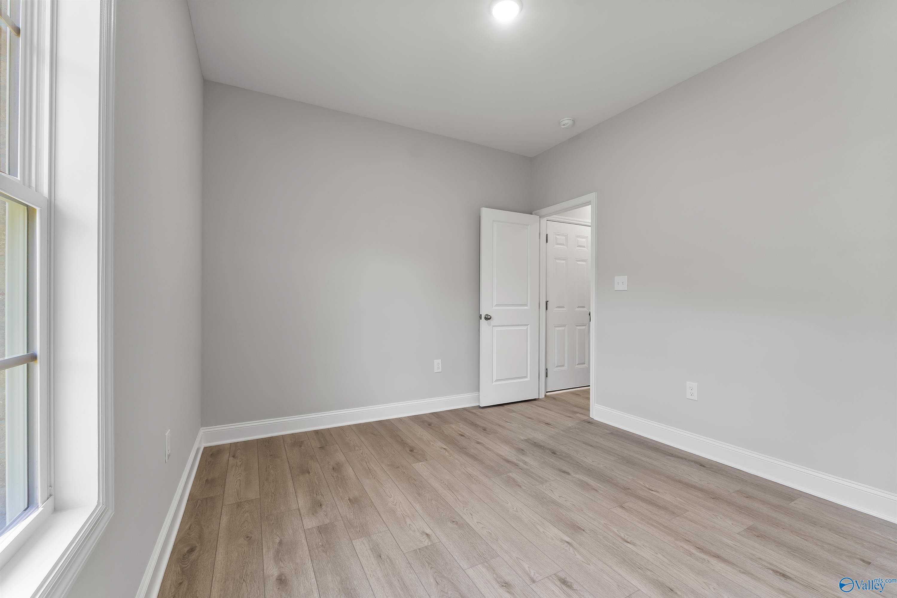 Spacious empty bedroom with gray walls, laminate wood floors, and large window in The Daphne C 4-bedroom home, Huntsville, AL