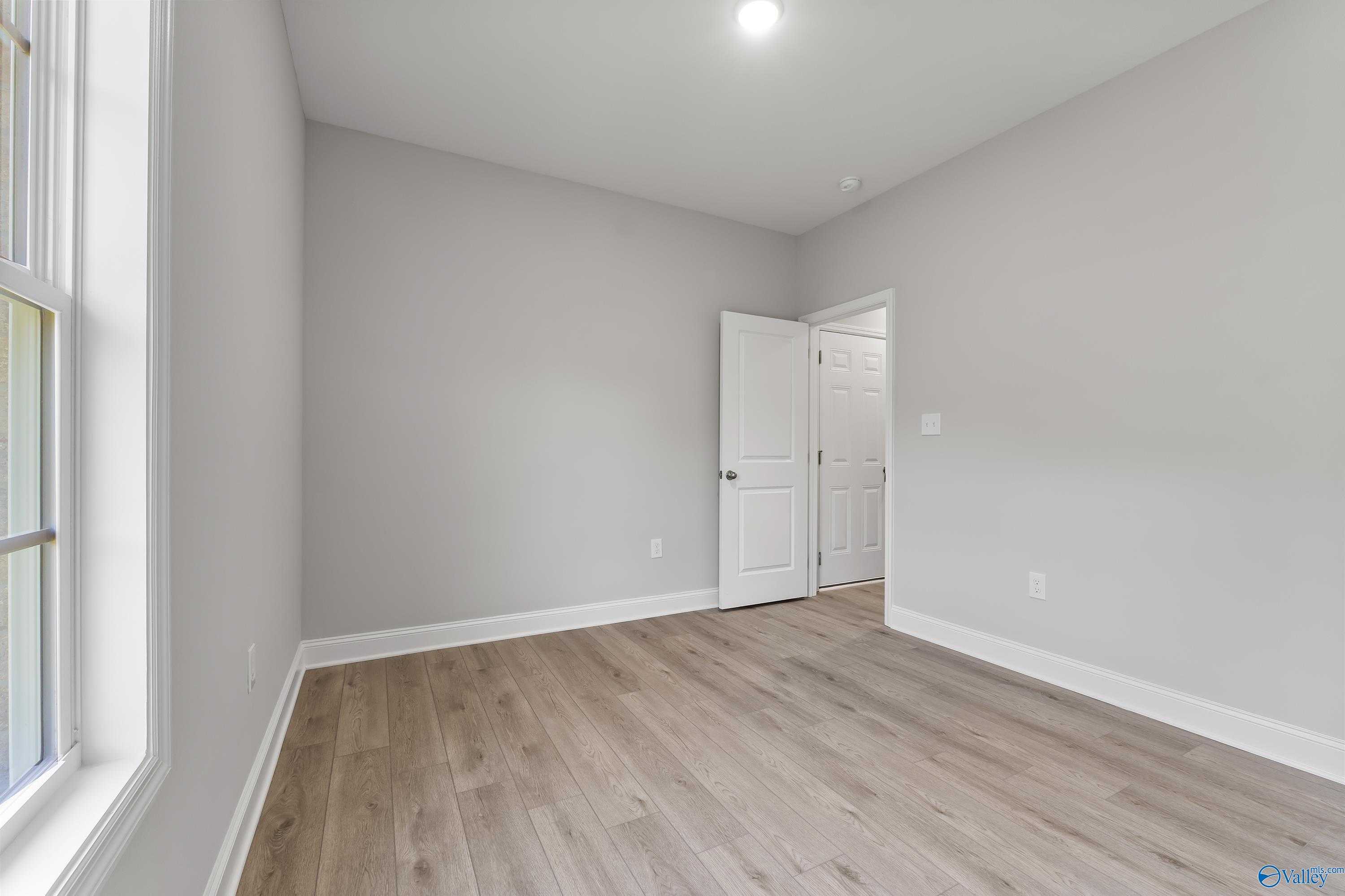 Spacious empty bedroom with gray walls, laminate wood floors, and large window in The Daphne C 4-bedroom home, Huntsville, AL