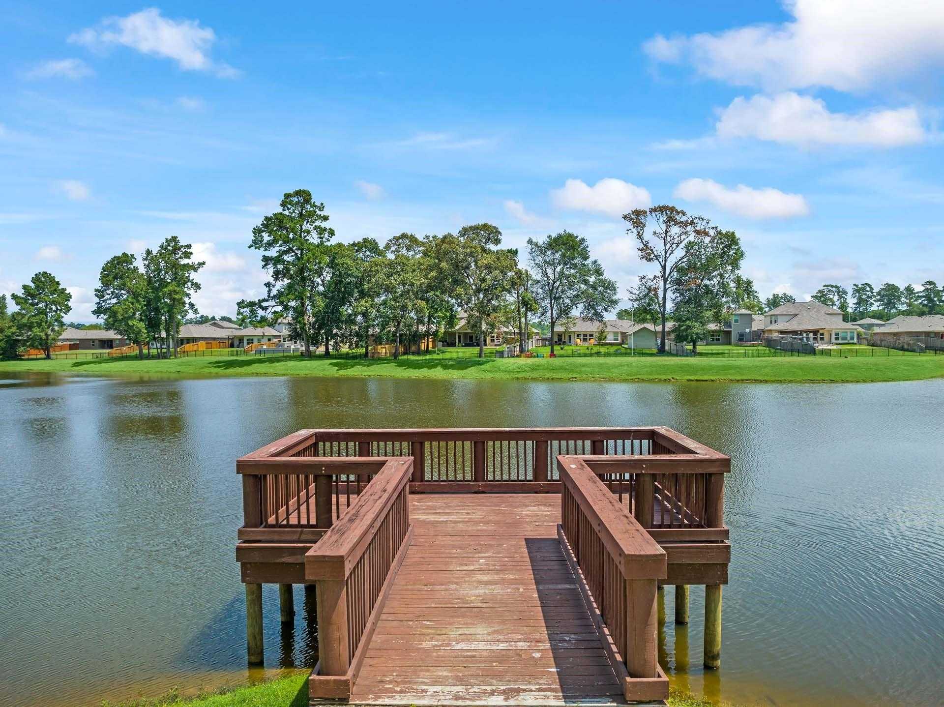 Scenic wooden pier over tranquil lake surrounded by pine trees and homes in Lakes at Black Oak, Magnolia, Texas