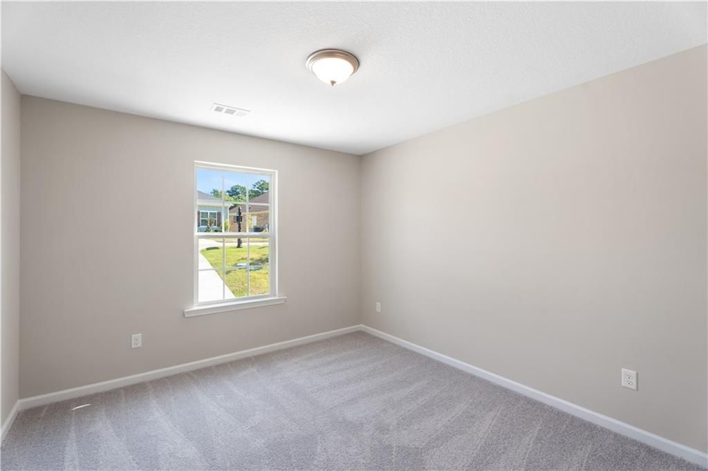 Bright secondary bedroom with beige walls, carpet flooring, and large window to lush yard in Davidson Homes The Washington, Phenix City