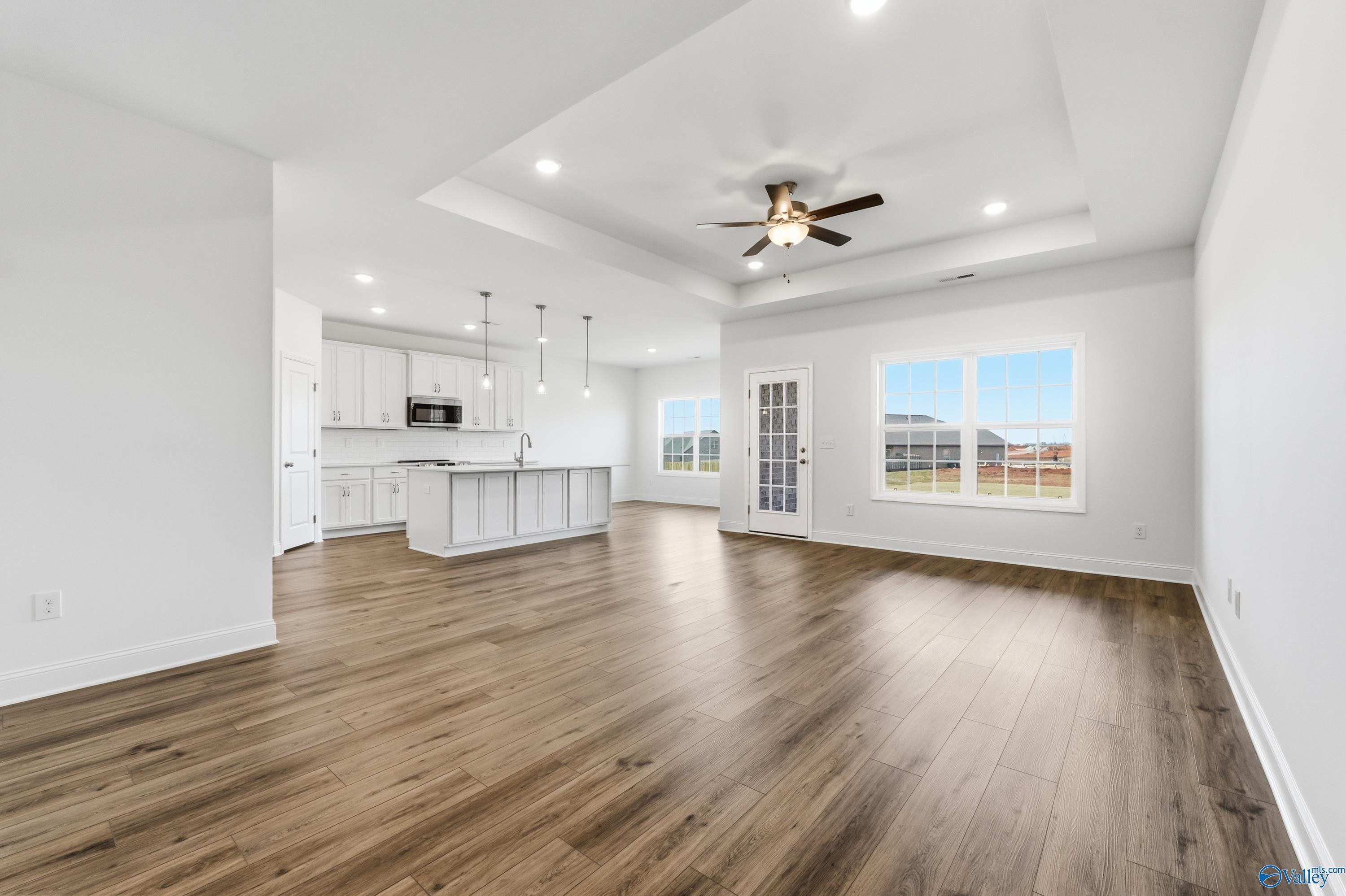 Open-concept kitchen and living space with white cabinets, island, hardwood floors, ceiling fan, and large windows in Davidson Homes The Montgomery C, Harvest, Alabama