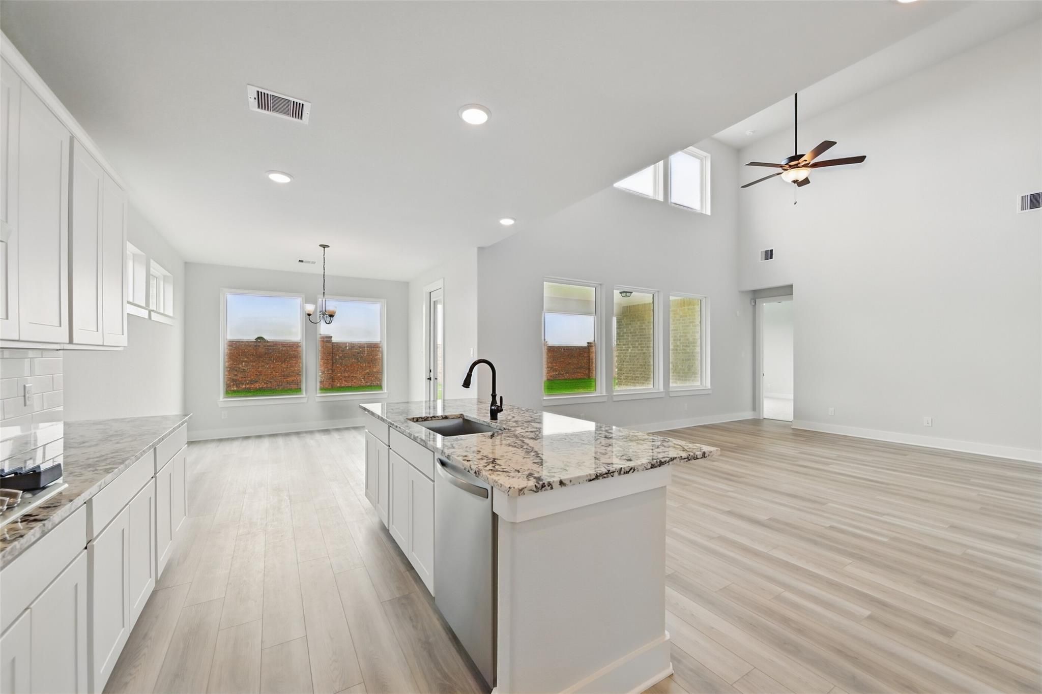 Modern open-concept kitchen with white cabinets, granite countertops, island sink, and backyard views in Davidson Homes The Victoria C, Lago Mar
