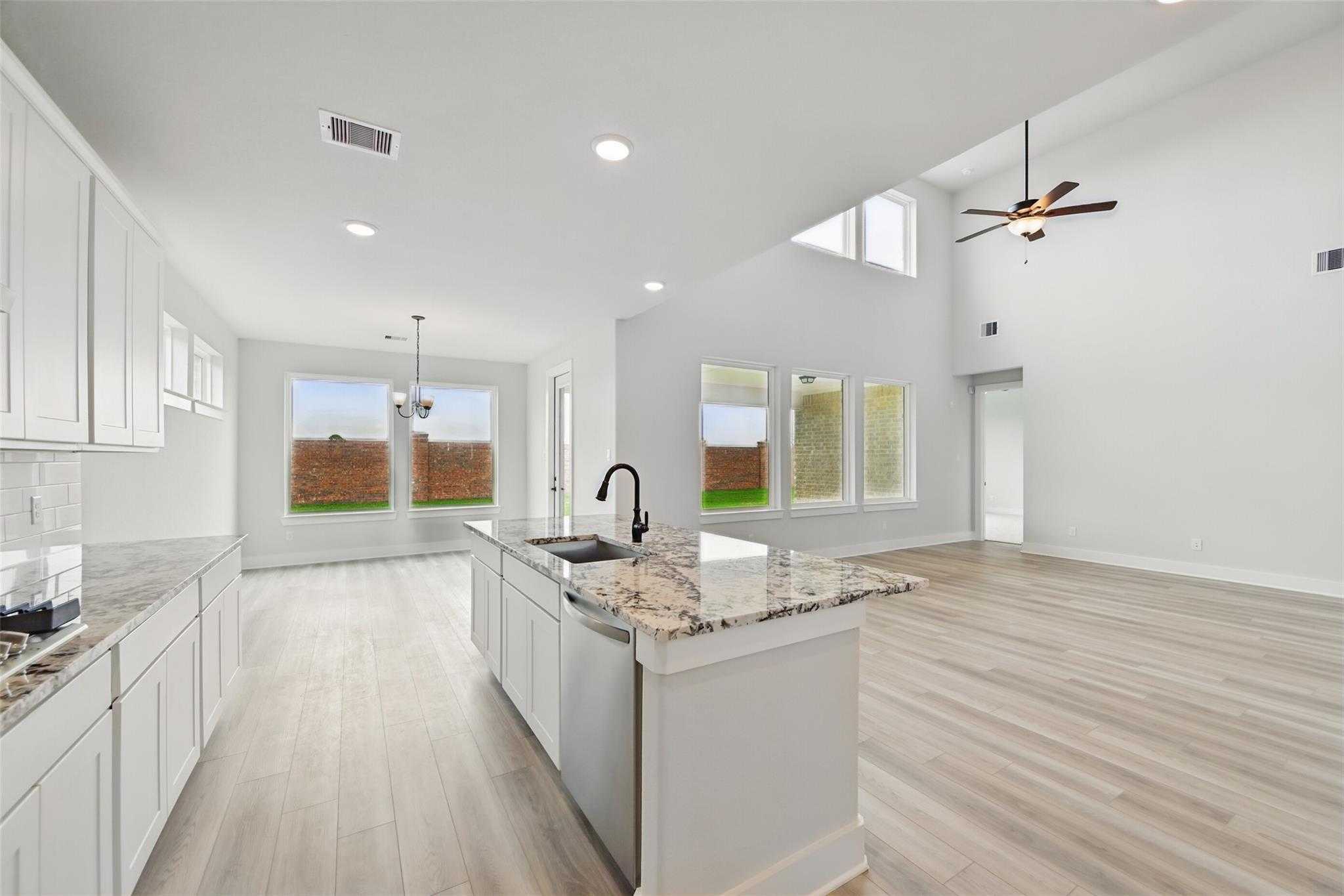 Modern open kitchen with white cabinets, granite island, large windows overlooking backyard in Davidson Homes The Victoria C, Texas City