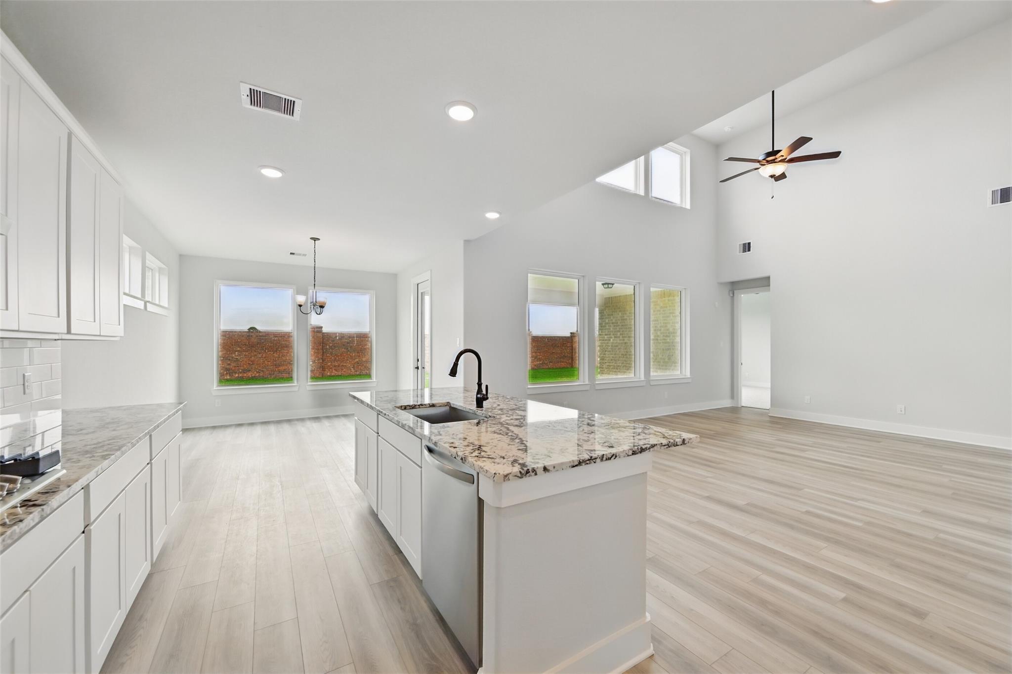 Modern open-concept kitchen with white cabinets, granite countertops, island sink, and backyard views in Davidson Homes The Victoria C, Lago Mar