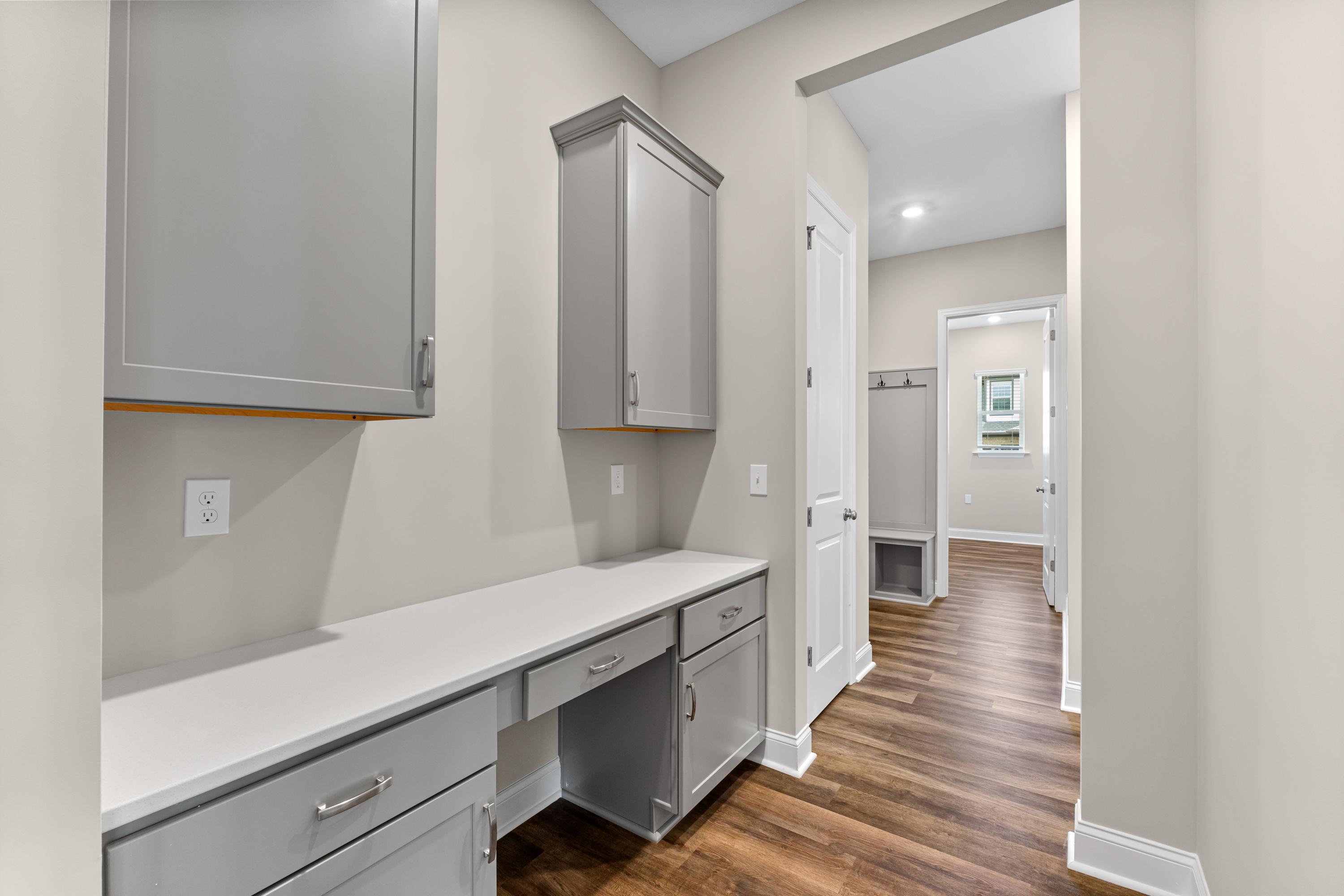Spacious laundry room in The Arcadia B featuring gray shaker cabinets, white countertop, and wood flooring