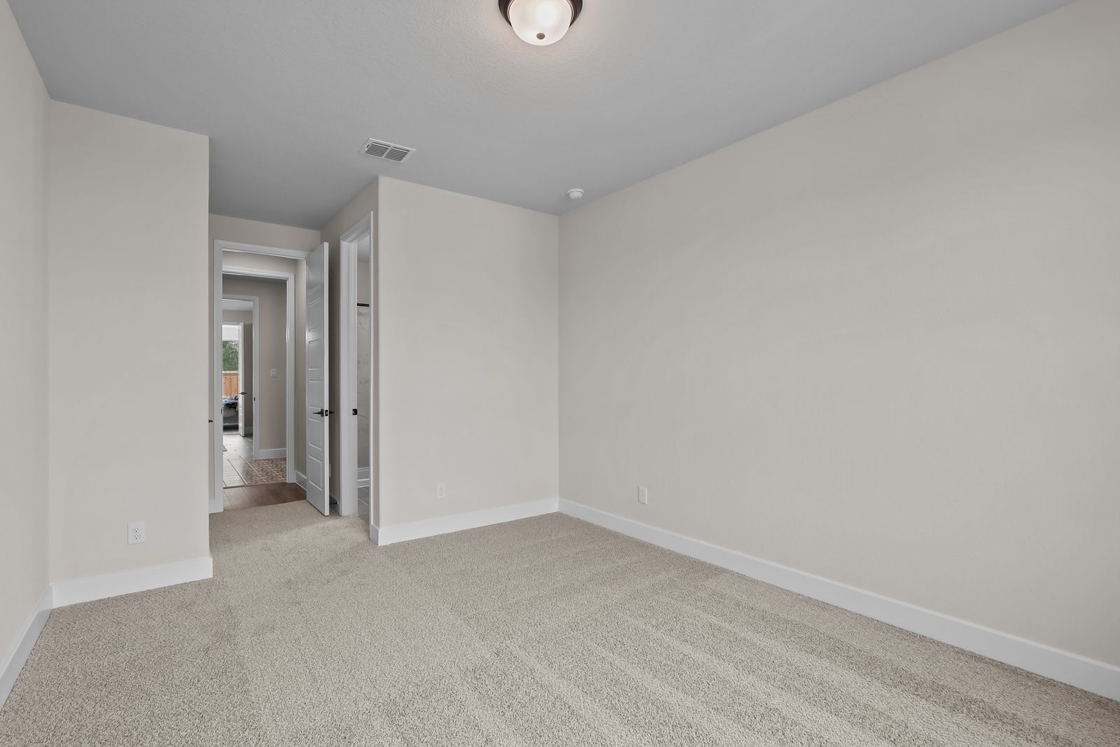 Spacious bedroom in The Belmont home design in Castroville, featuring neutral carpeting and hallway views.