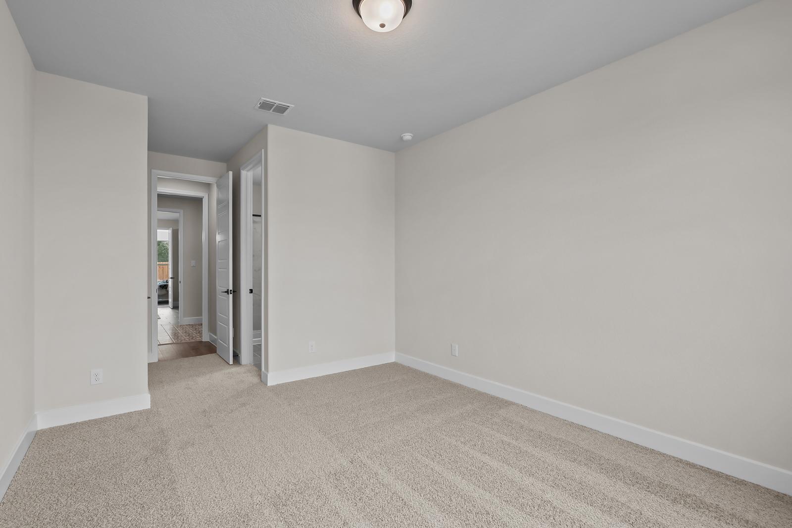 Spacious bedroom in The Belmont home design in Castroville, featuring neutral carpeting and hallway views.