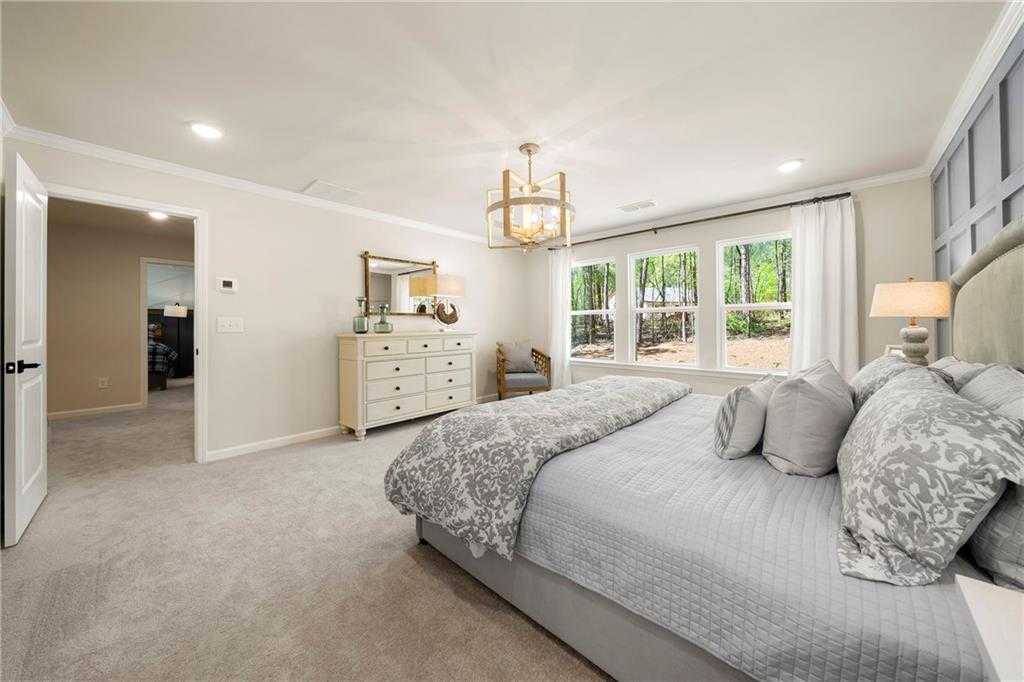 Elegant master bedroom with king bed, gray headboard, chandelier, and wooded views in Davidson Homes The Hickory B, Riverwood, Dallas, Georgia