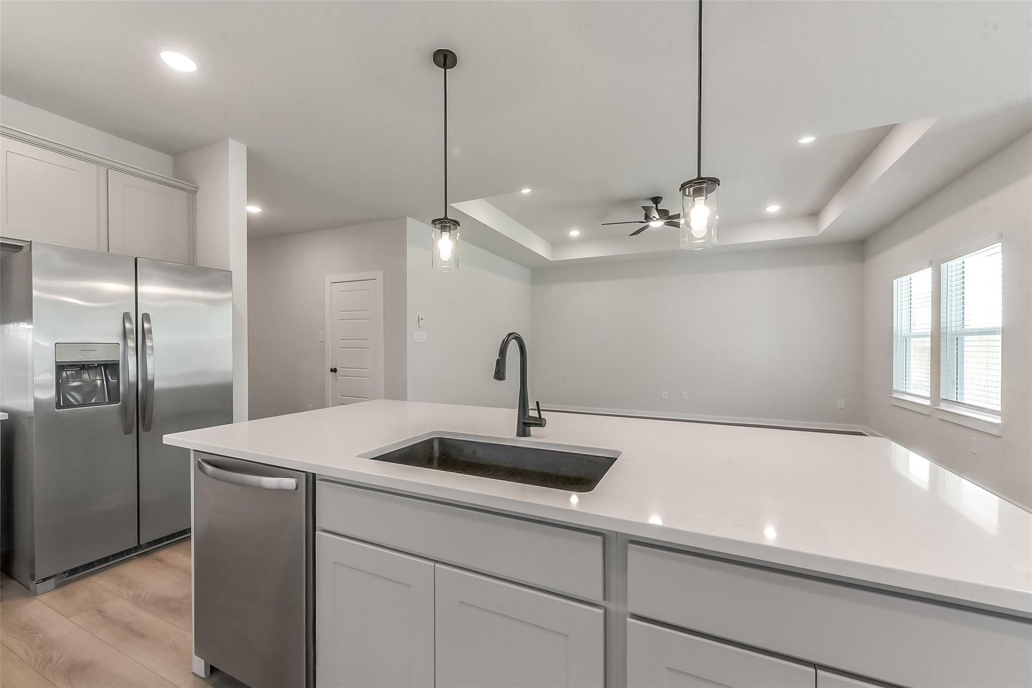 Modern kitchen with white quartz island, stainless steel fridge and dishwasher, pendant lights in Davidson Homes The Everett C, Crosby, Texas