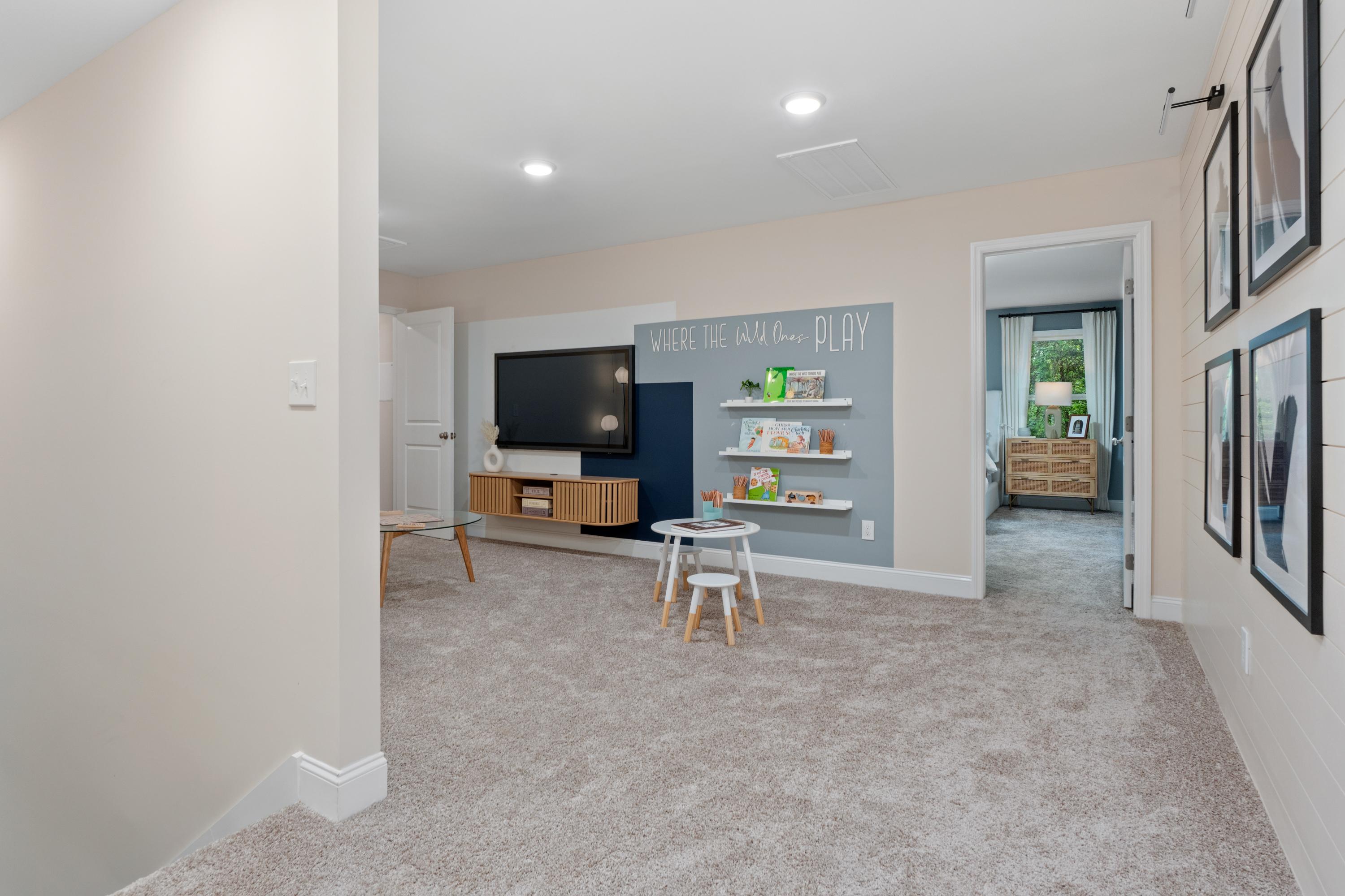 Cozy children's playroom in Pavilion Huntsville AL by Davidson Homes featuring "Learn Play" wall, toy shelves, TV and kids' table