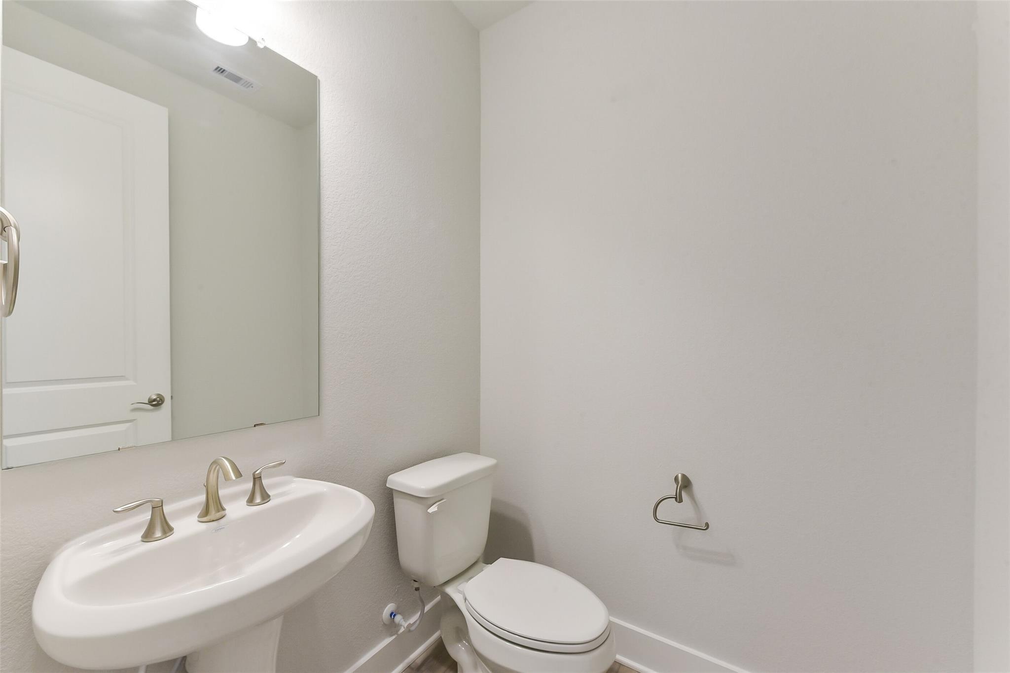 Modern half bathroom with white vanity sink, chrome faucet, mirror, and toilet in Davidson Homes The Edward A, Lago Mar, Texas City