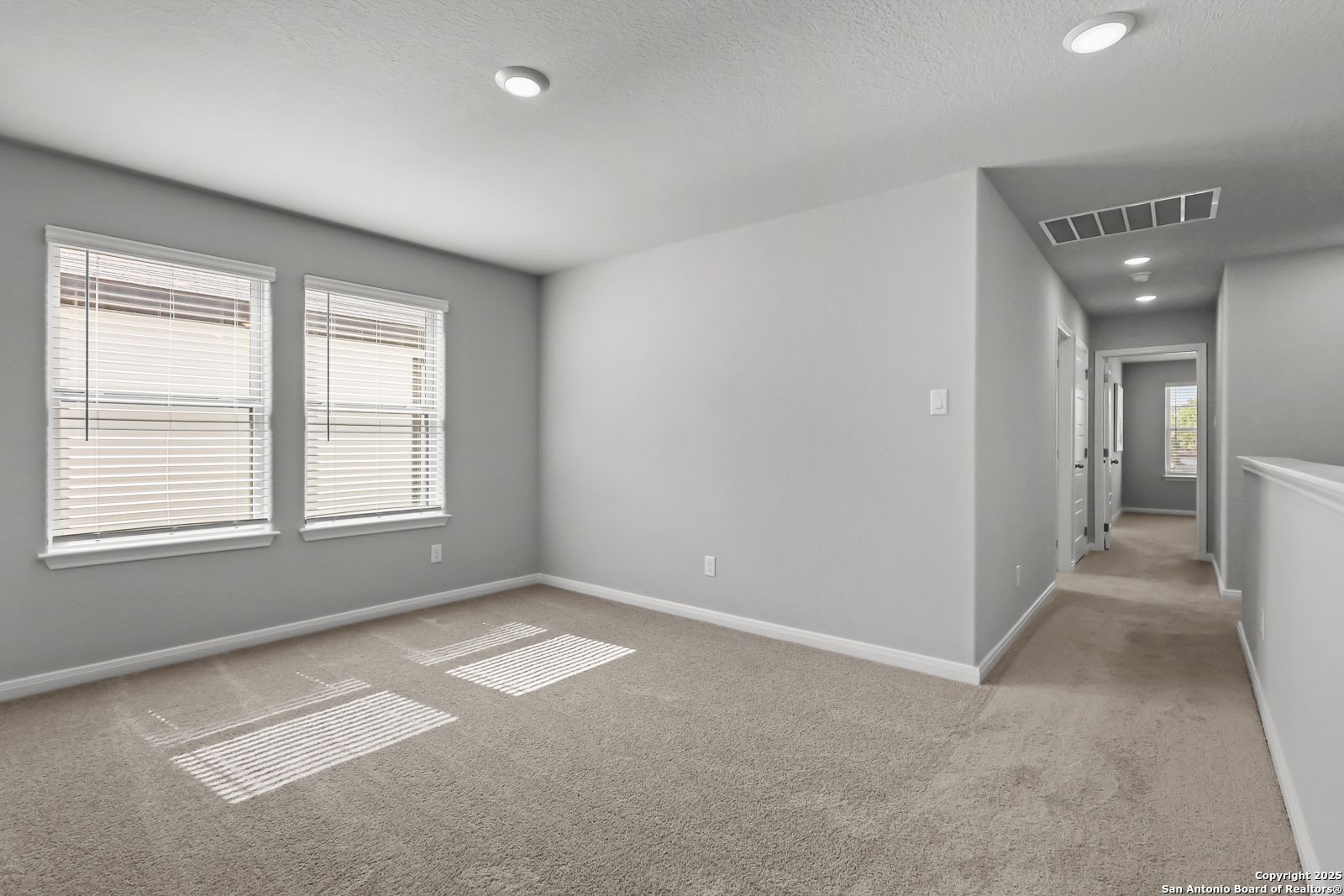 Spacious upstairs bedroom with gray walls, beige carpet, large windows and hallway in 5-bedroom The Gillian C home, Davidson Homes, San Antonio TX