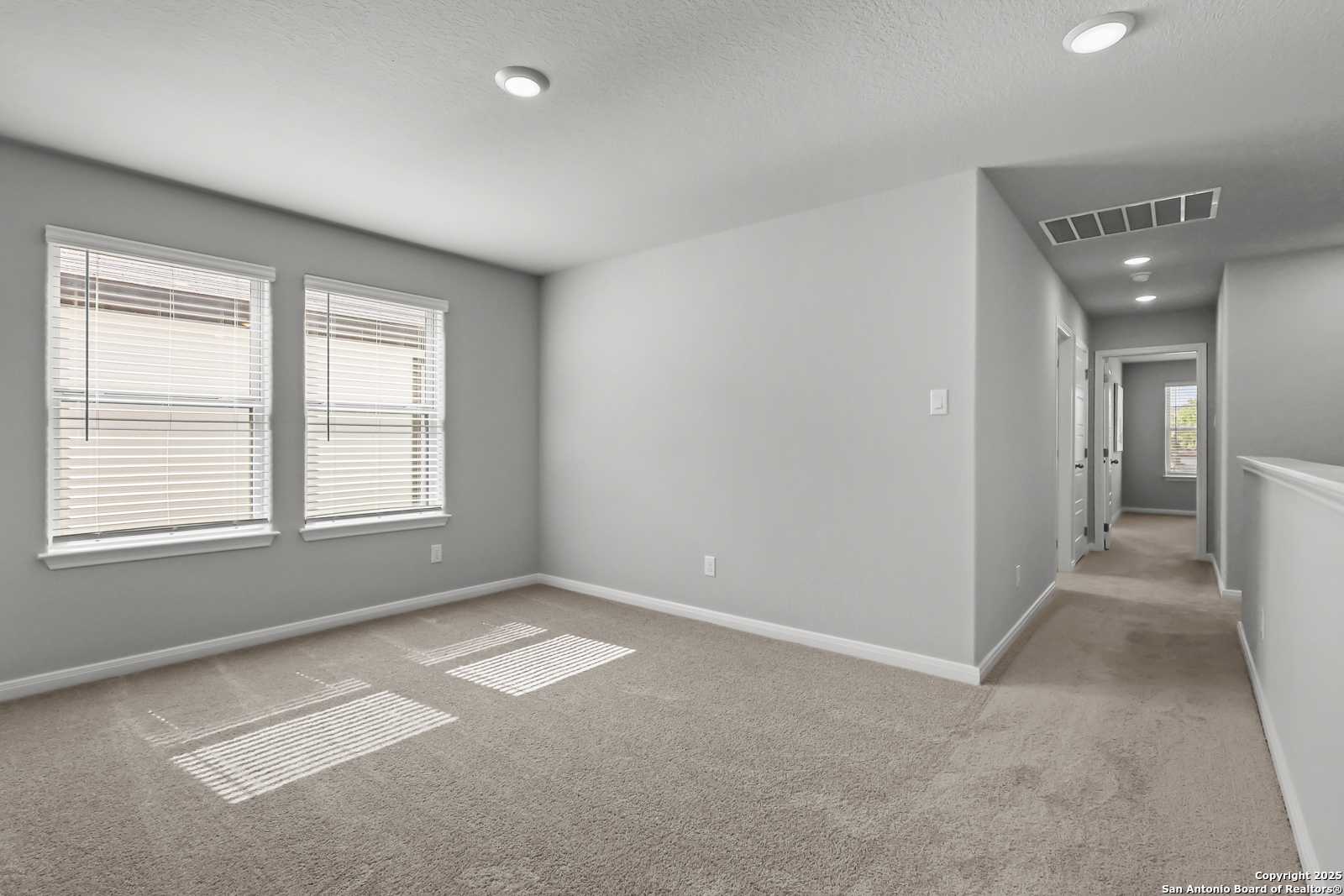 Spacious upstairs bedroom with gray walls, beige carpet, large windows and hallway in 5-bedroom The Gillian C home, Davidson Homes, San Antonio TX
