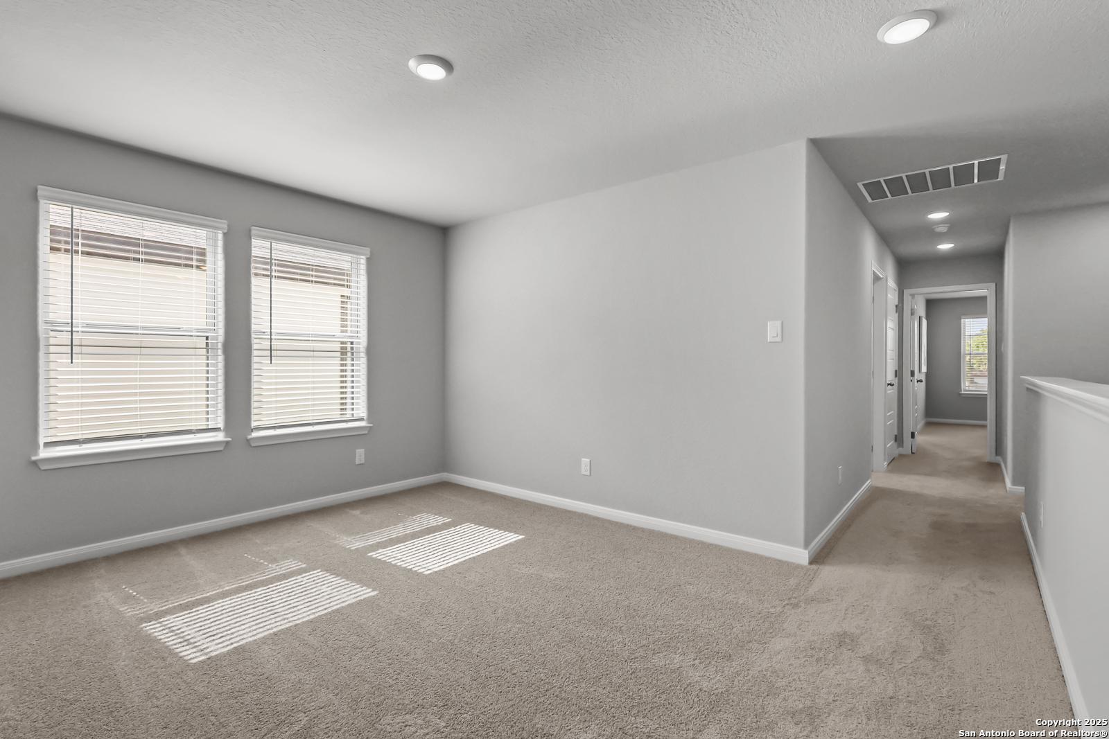 Spacious upstairs bedroom with gray walls, beige carpet, large windows and hallway in 5-bedroom The Gillian C home, Davidson Homes, San Antonio TX