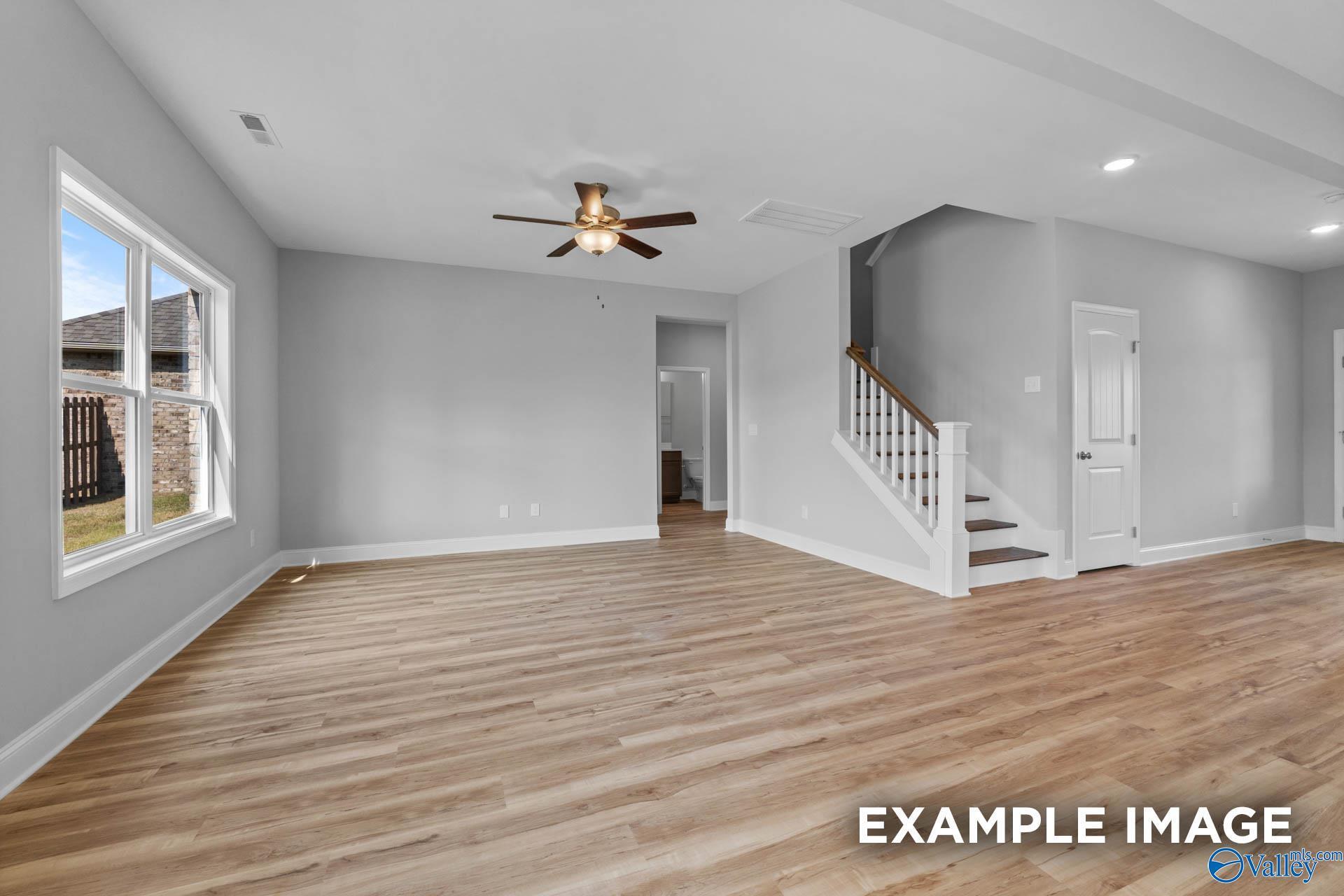 Spacious living room with wood-style flooring and staircase in The Shelby B floor plan at Walker's Hill, Meridianville.
