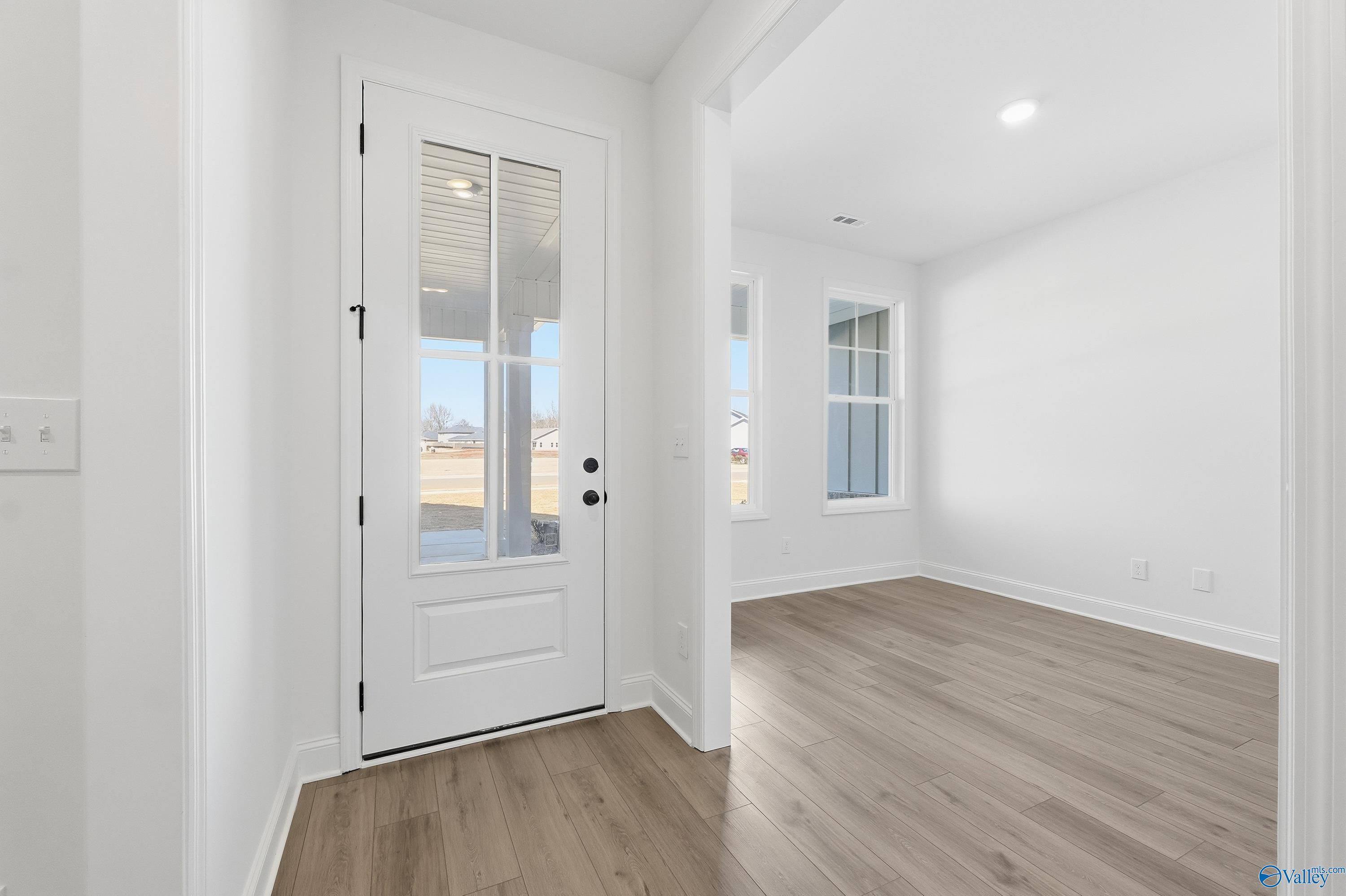 Bright entryway with white glass-paneled front door, sidelights, and light oak floors in Davidson Homes The Rockford D, Hazel Green, AL