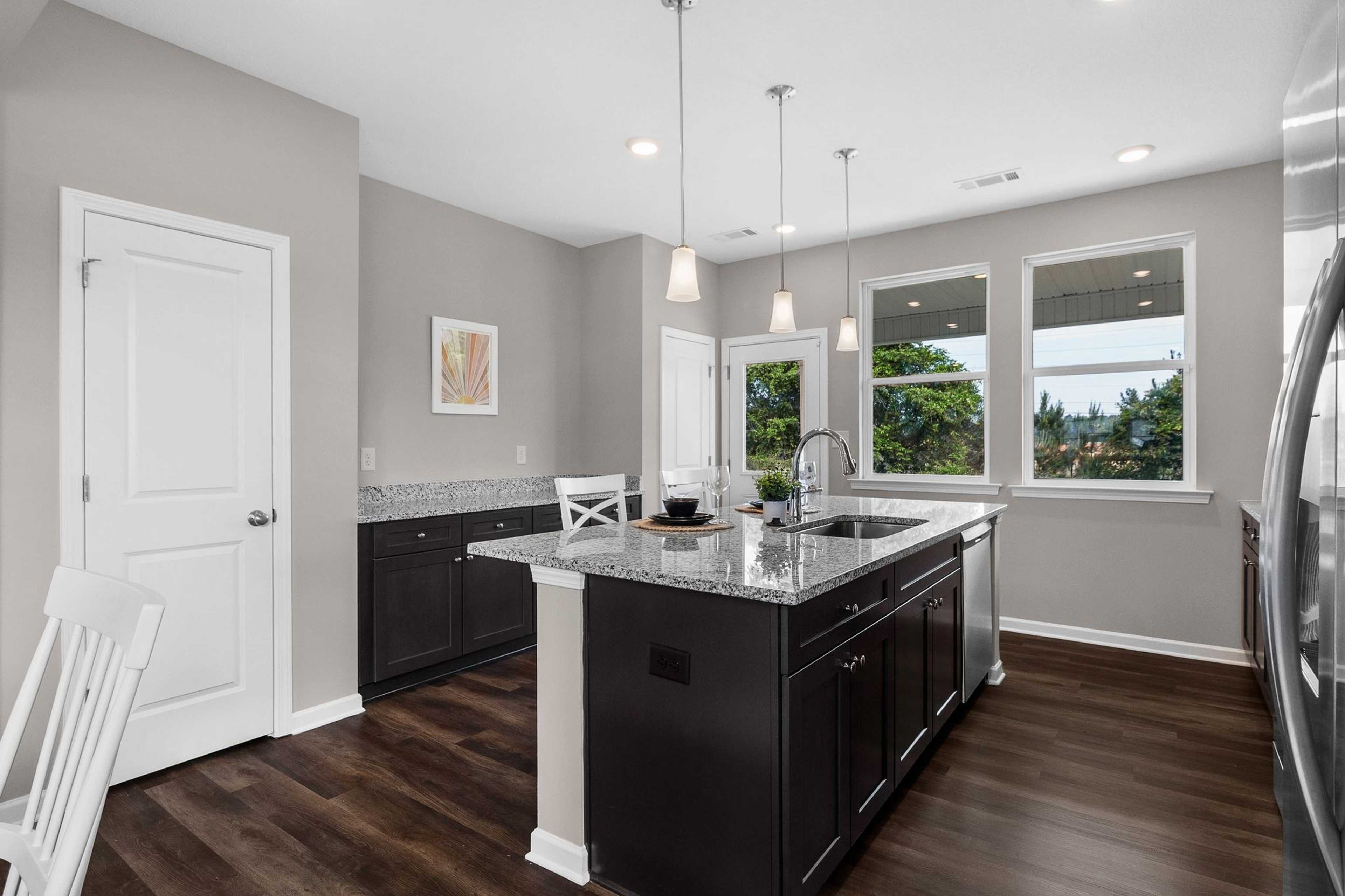 Spacious modern kitchen at Ivy Glen in Perry, Georgia with granite island, dark cabinets, hardwood floors, and large windows