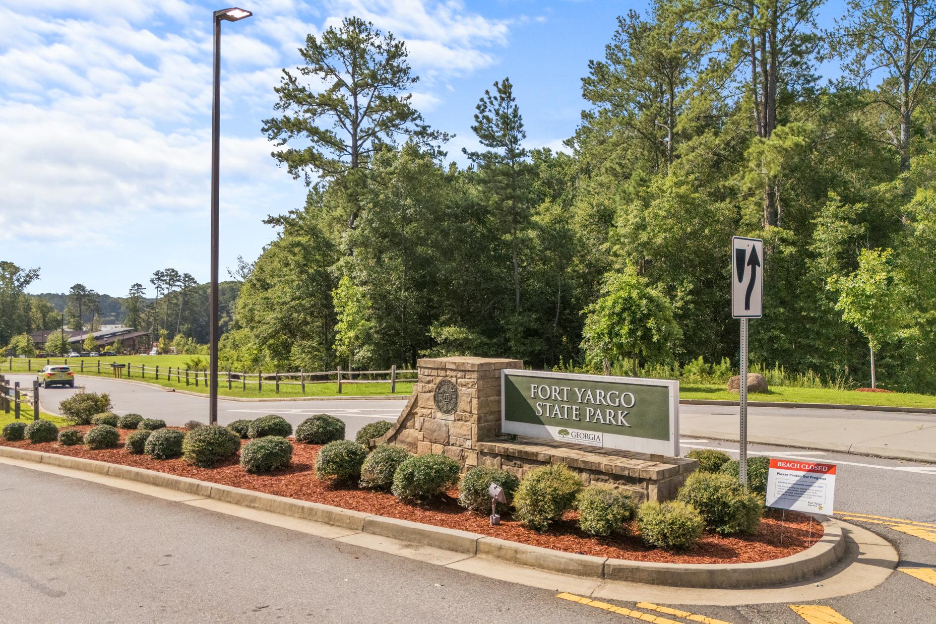 Lake Shore at Fort Yargo entrance sign in Winder GA with stone pillar, lush pines, shrubs, and curved roadway