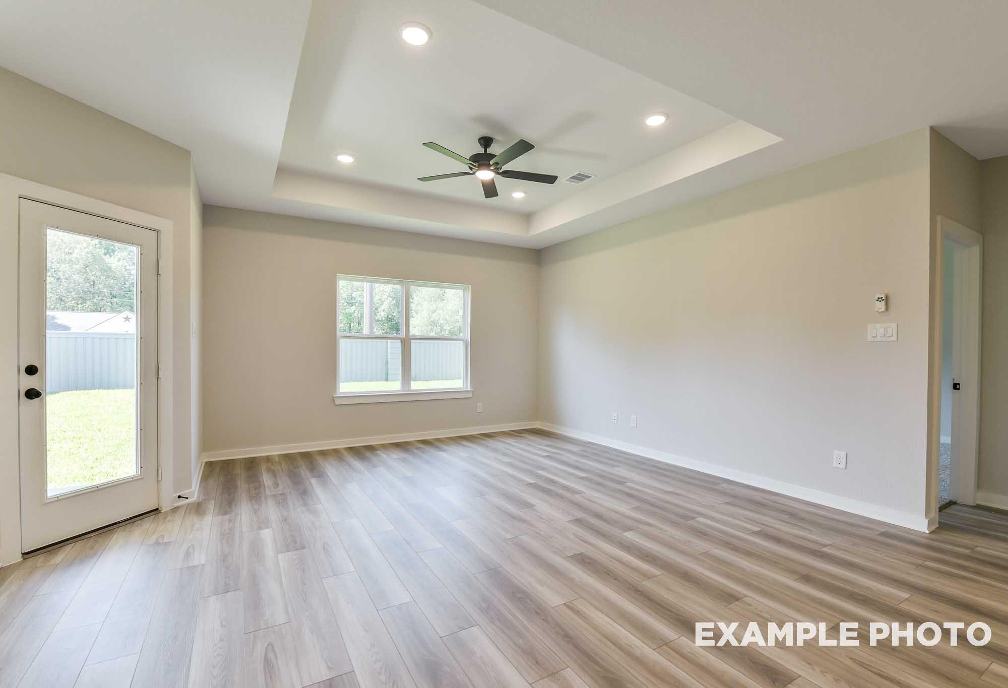 Spacious living room in The Daphne F with tray ceiling, ceiling fan, large windows, French doors to backyard, and light wood floors in Crosby TX home