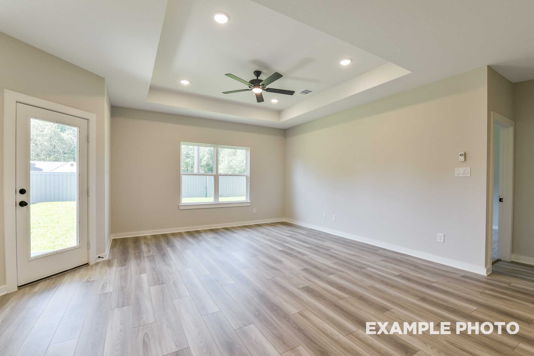 Spacious family room in The Daphne G with tray ceiling, ceiling fan, large windows, French door to backyard, and hardwood floors
