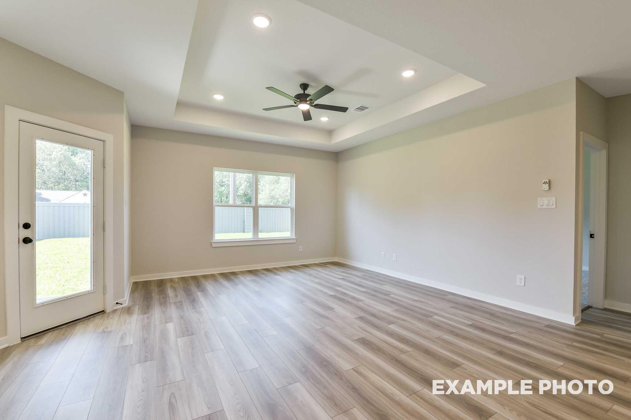 Spacious family room in The Daphne G with tray ceiling, ceiling fan, large windows, French door to backyard, and hardwood floors
