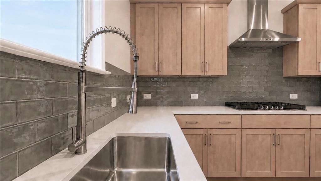 Modern kitchen with light wood cabinets, gray subway tile backsplash, and stainless steel sink in Wehunt Meadows home.