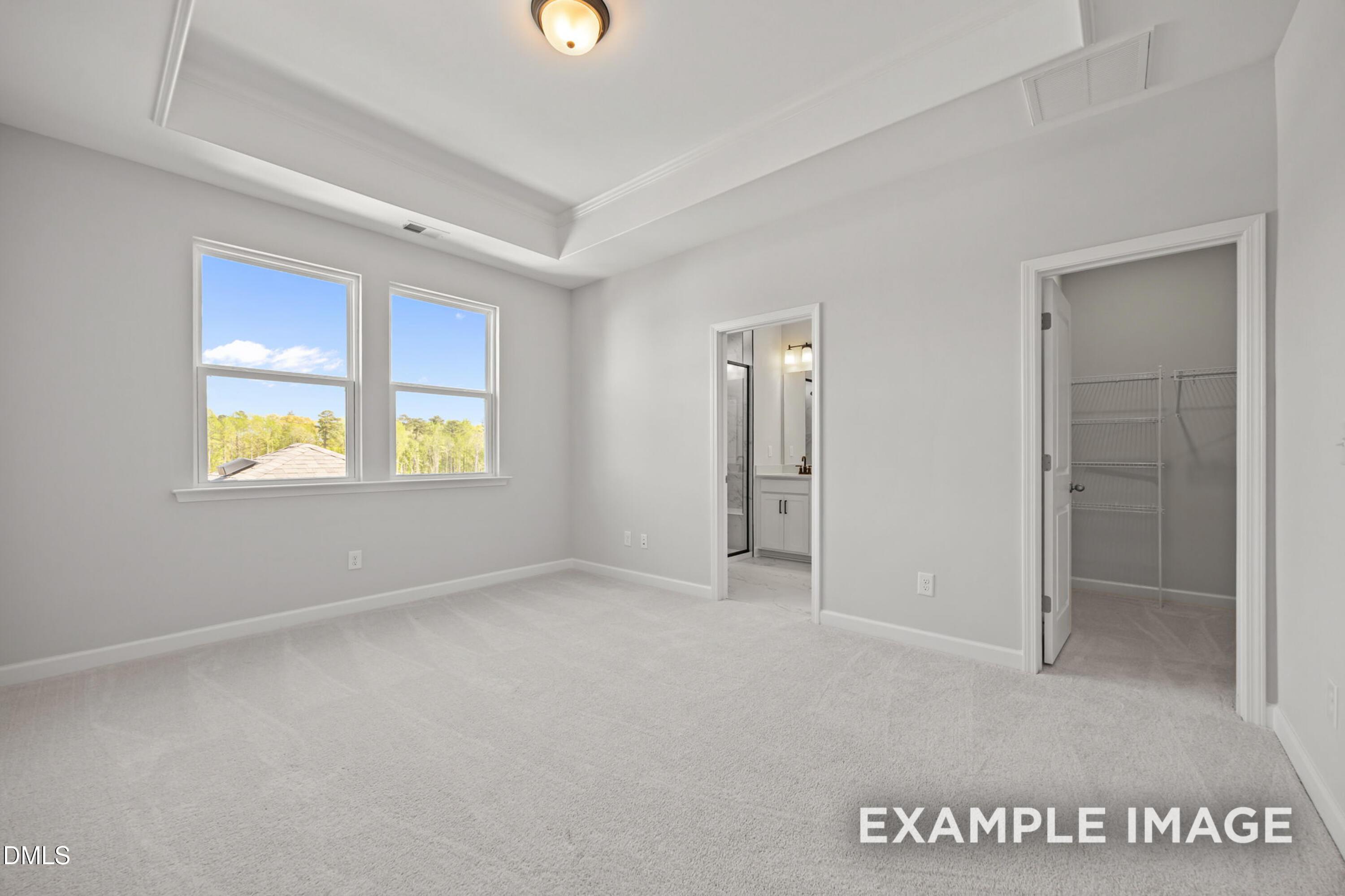 Primary bedroom with tray ceiling, en-suite bath, and walk-in closet in The Alexander B at Forestville Yard, Knightdale, NC.