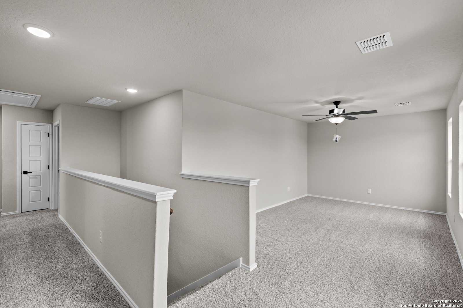 Spacious upstairs hallway with beige walls, carpeted floors, ceiling fan, and railing in Davidson Homes The Murray I, San Antonio, Texas