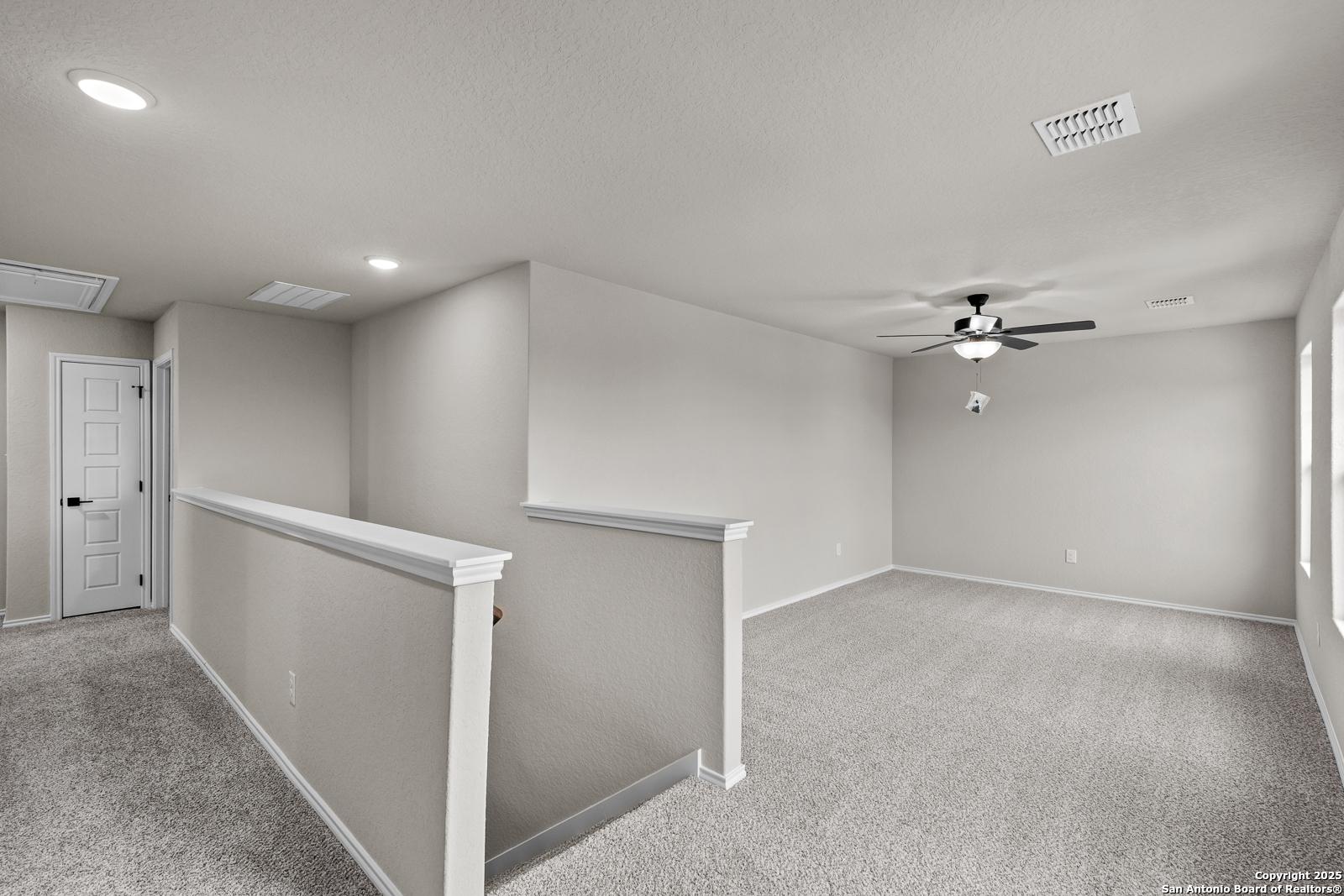 Spacious upstairs hallway with beige walls, carpeted floors, ceiling fan, and railing in Davidson Homes The Murray I, San Antonio, Texas