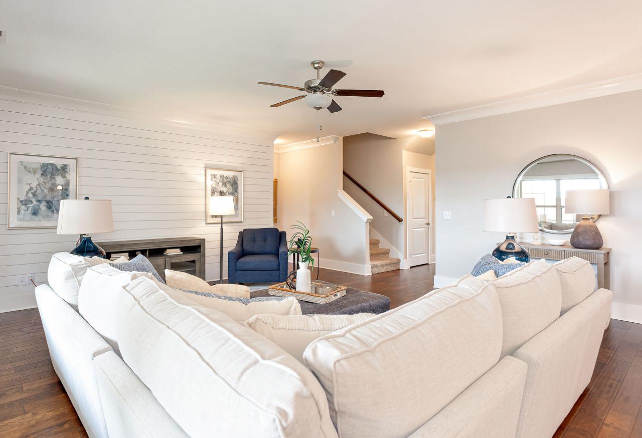 Spacious living room in The Rockford by Davidson Homes, white shiplap walls, L-shaped white sofa, blue armchair, hardwood floors, open staircase