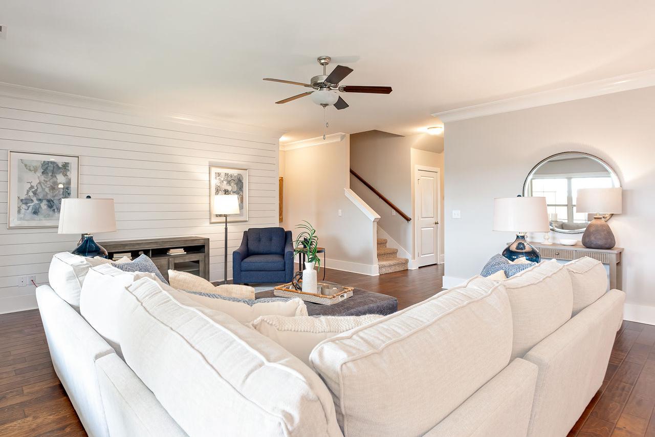 Spacious living room in The Rockford by Davidson Homes, white shiplap walls, L-shaped white sofa, blue armchair, hardwood floors, open staircase
