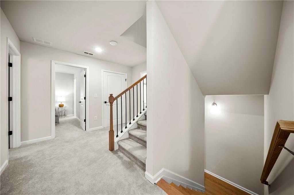 Bright upstairs hallway with wooden staircase, carpeted steps, and bedroom doors in Davidson Homes The Hickory B, Riverwood, GA