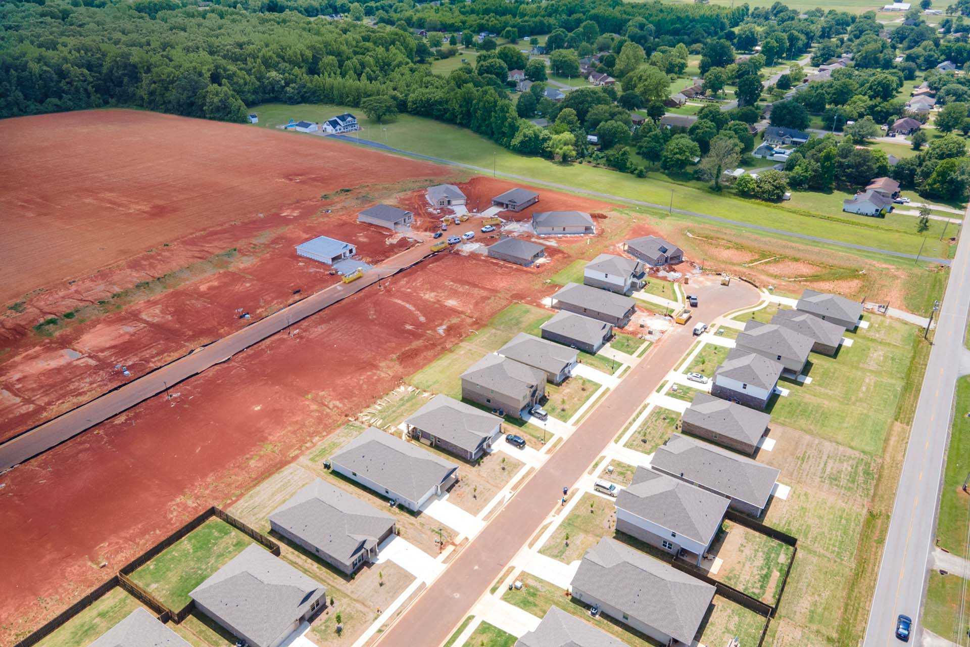 Aerial view of Clearview neighborhood in Hazel Green Alabama with new single-story homes, red clay construction site and wooded fields