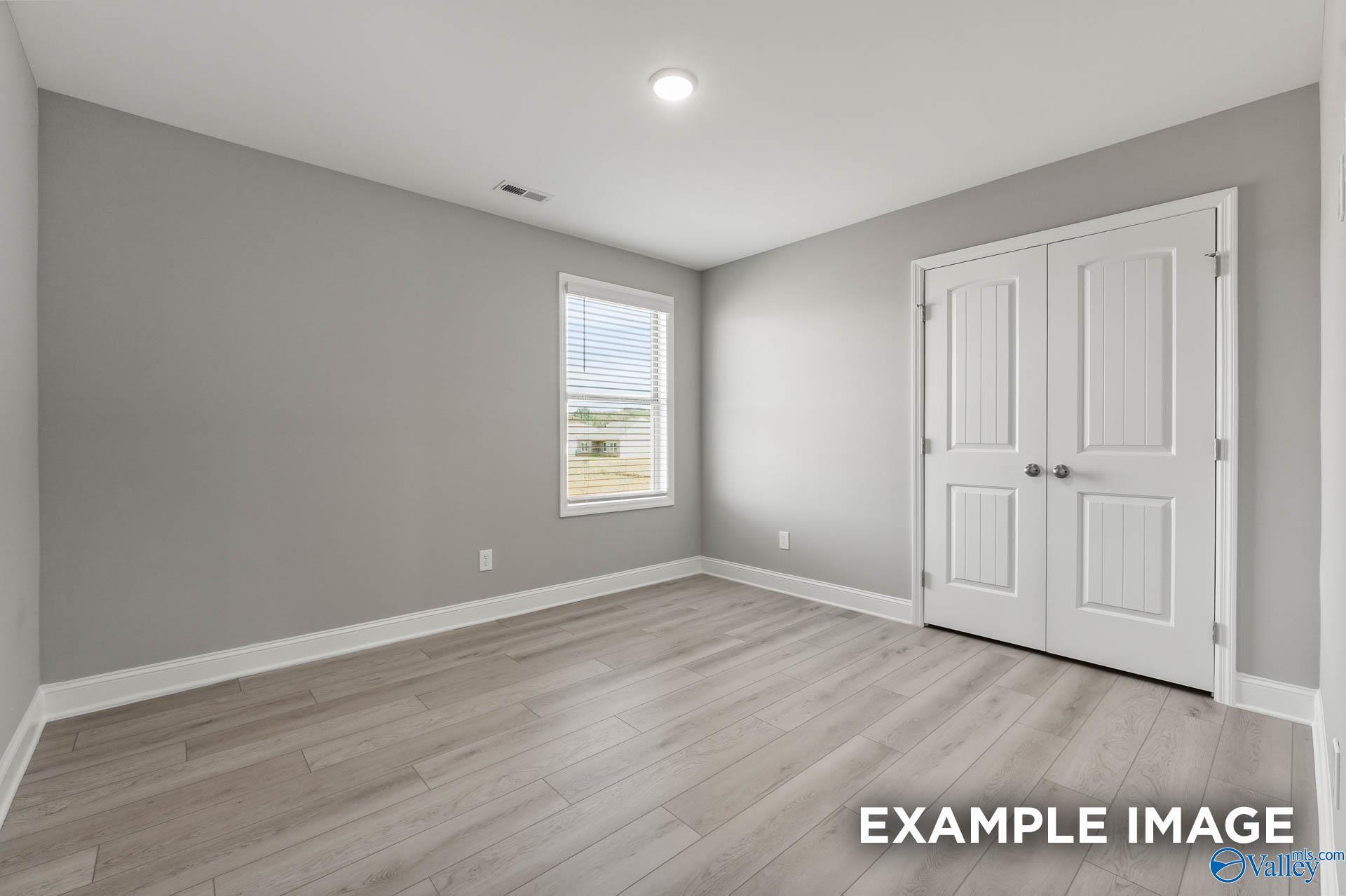 Spacious bedroom with gray walls, double closet doors, window blinds, and light laminate flooring in Davidson Homes The Everett B, Toney, Alabama