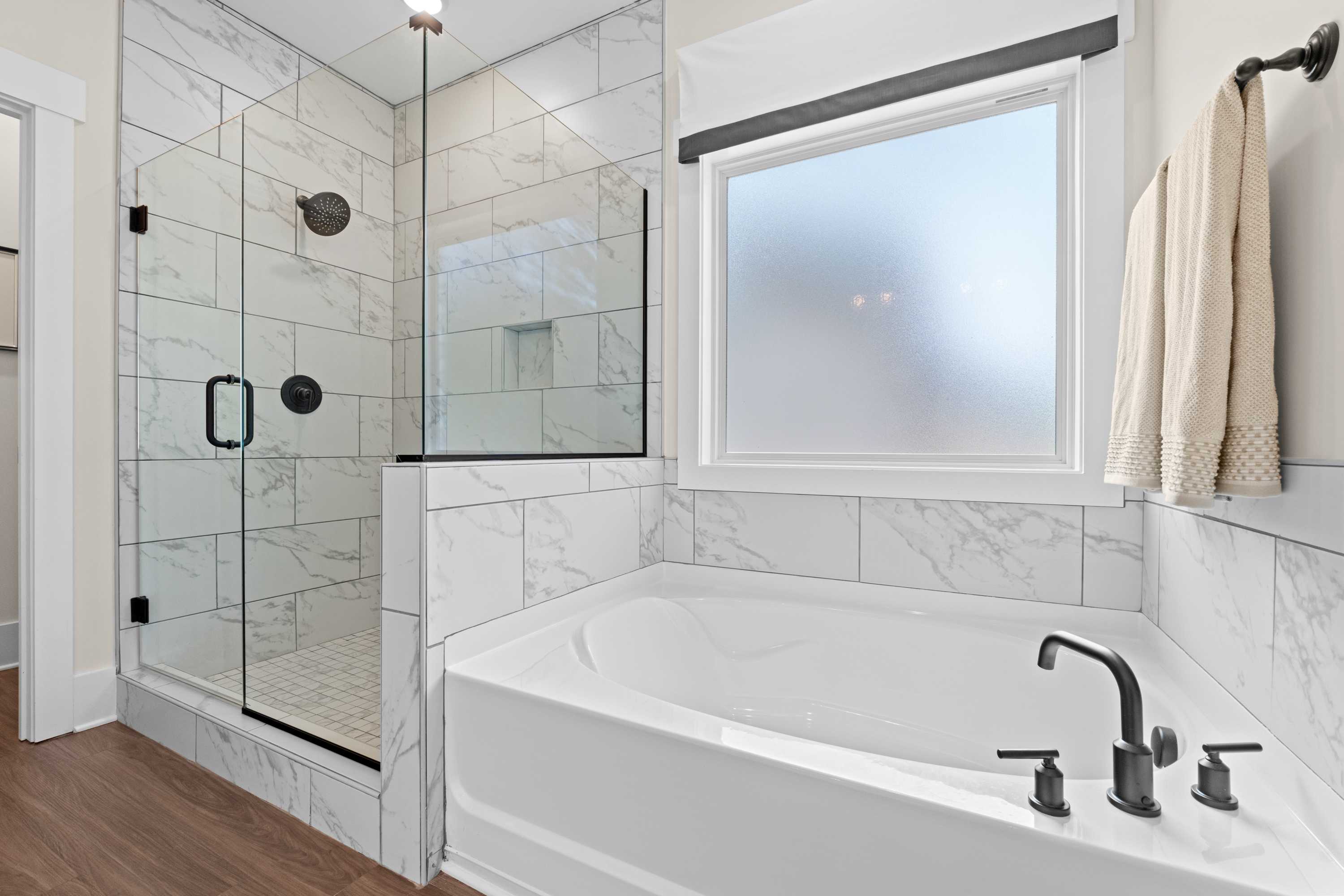 Elegant primary bathroom at Ivy Hills in Toney, Alabama with white subway tile, glass walk-in shower, and corner soaking tub