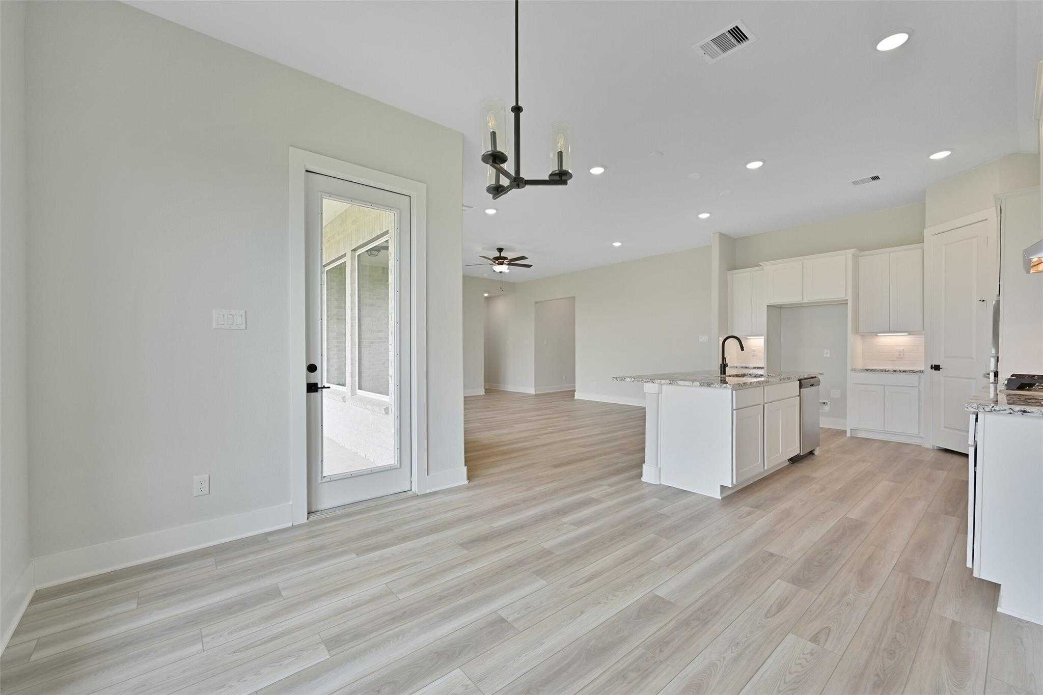 Open-concept kitchen with white cabinets, island sink, and glass French doors to screened porch in Davidson Homes The Edward C, Lago Mar, Texas City