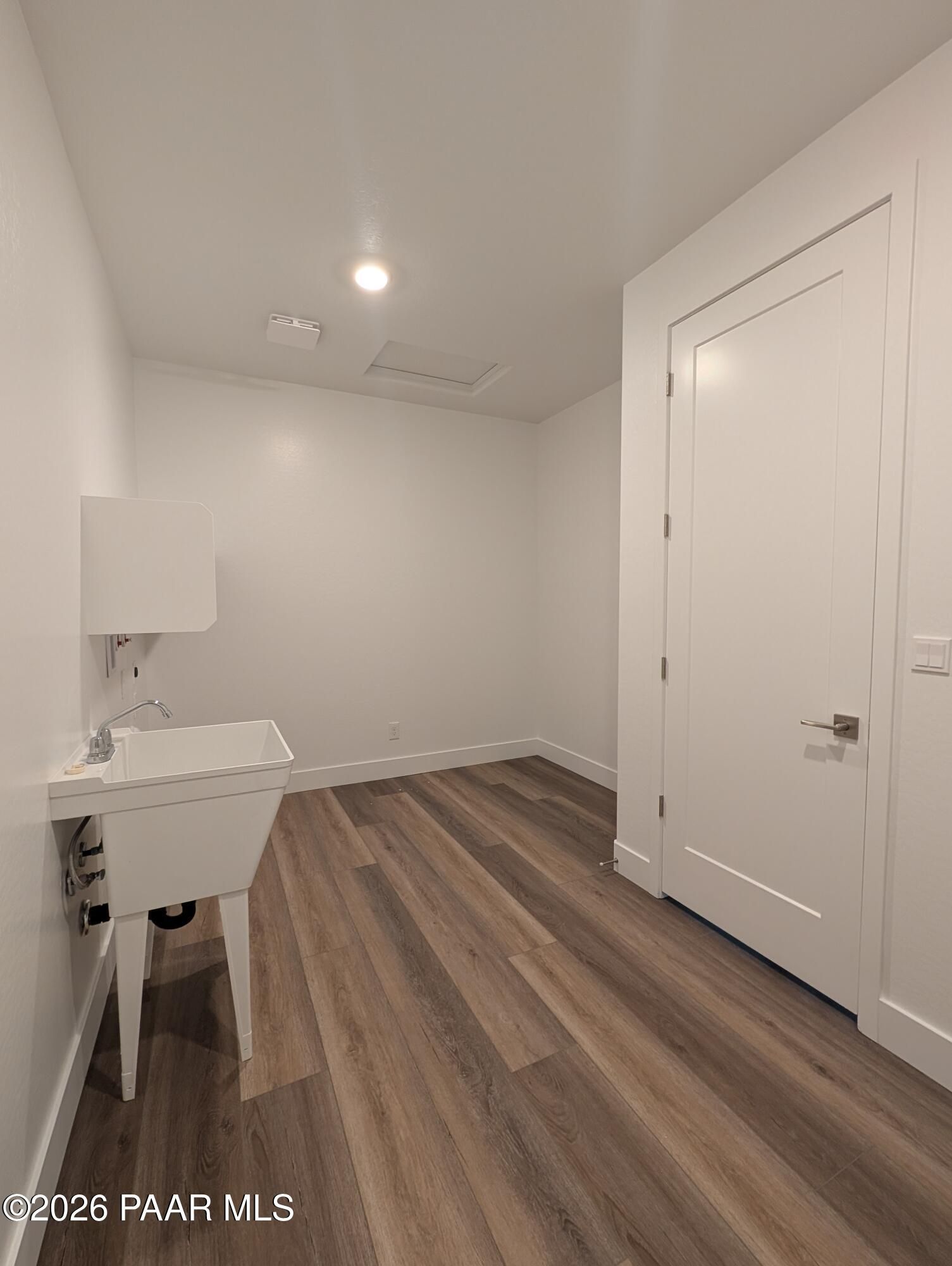 Bright laundry room with white utility sink, cabinet, and laminate wood flooring in Davidson Homes Durango II F, Prescott, AZ