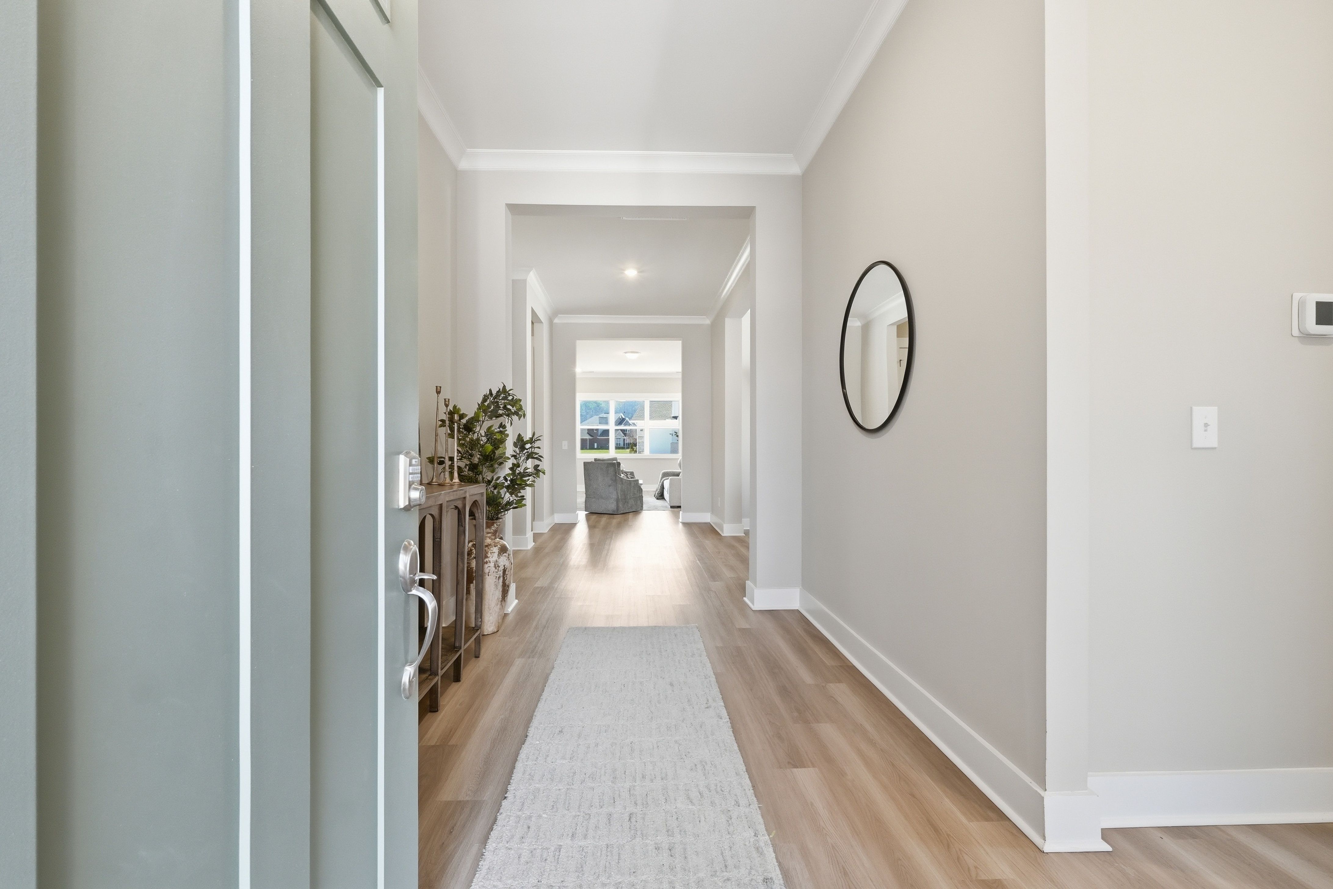 Spacious foyer hallway at The Meadows at Hampton Cove in Owens Cross Roads AL with light oak floors, beige walls, round mirror and console table