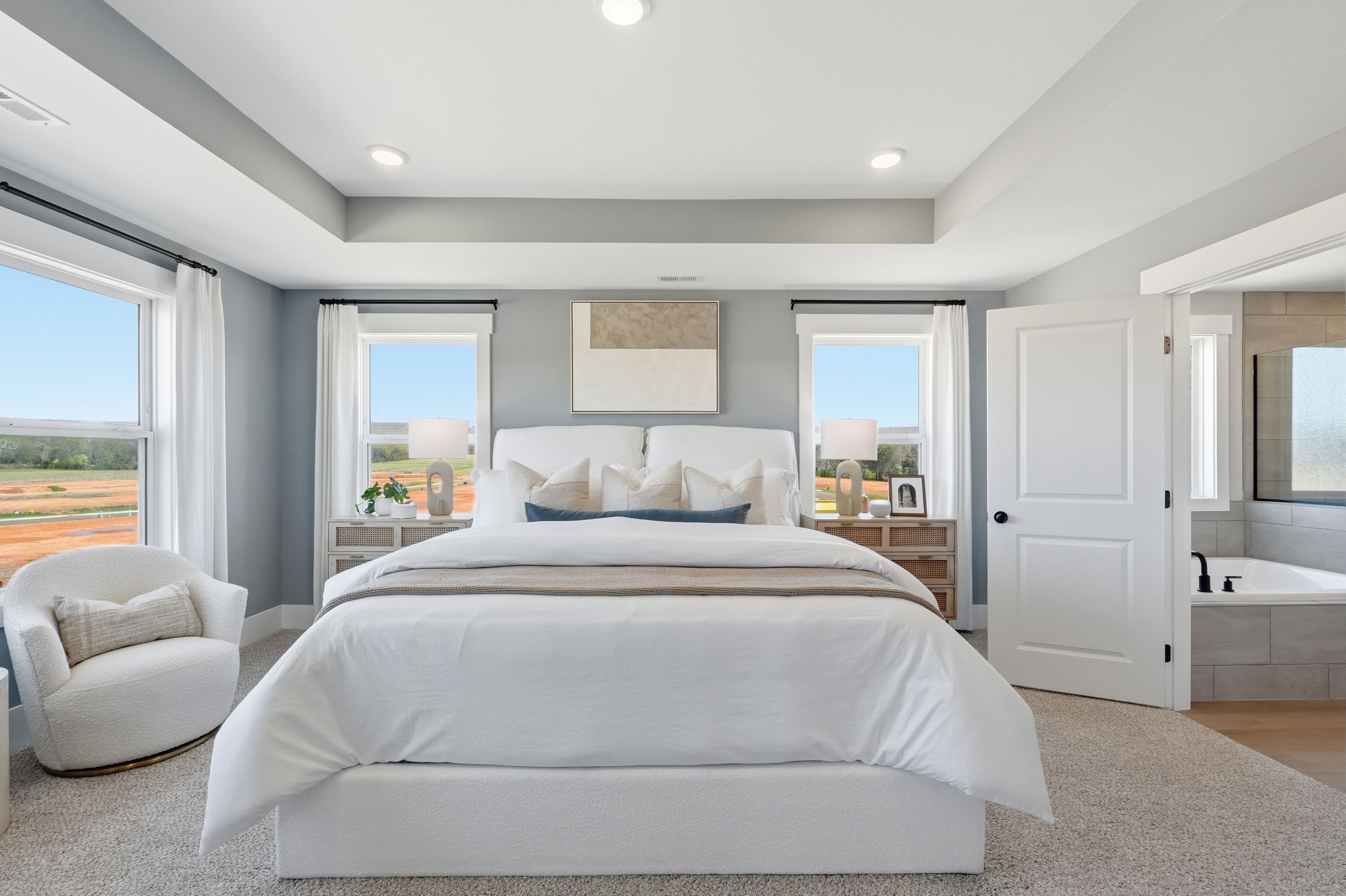 Modern primary bedroom in Berry Cove New Market AL with white king bed, gray walls, large windows, and en-suite tub bathroom