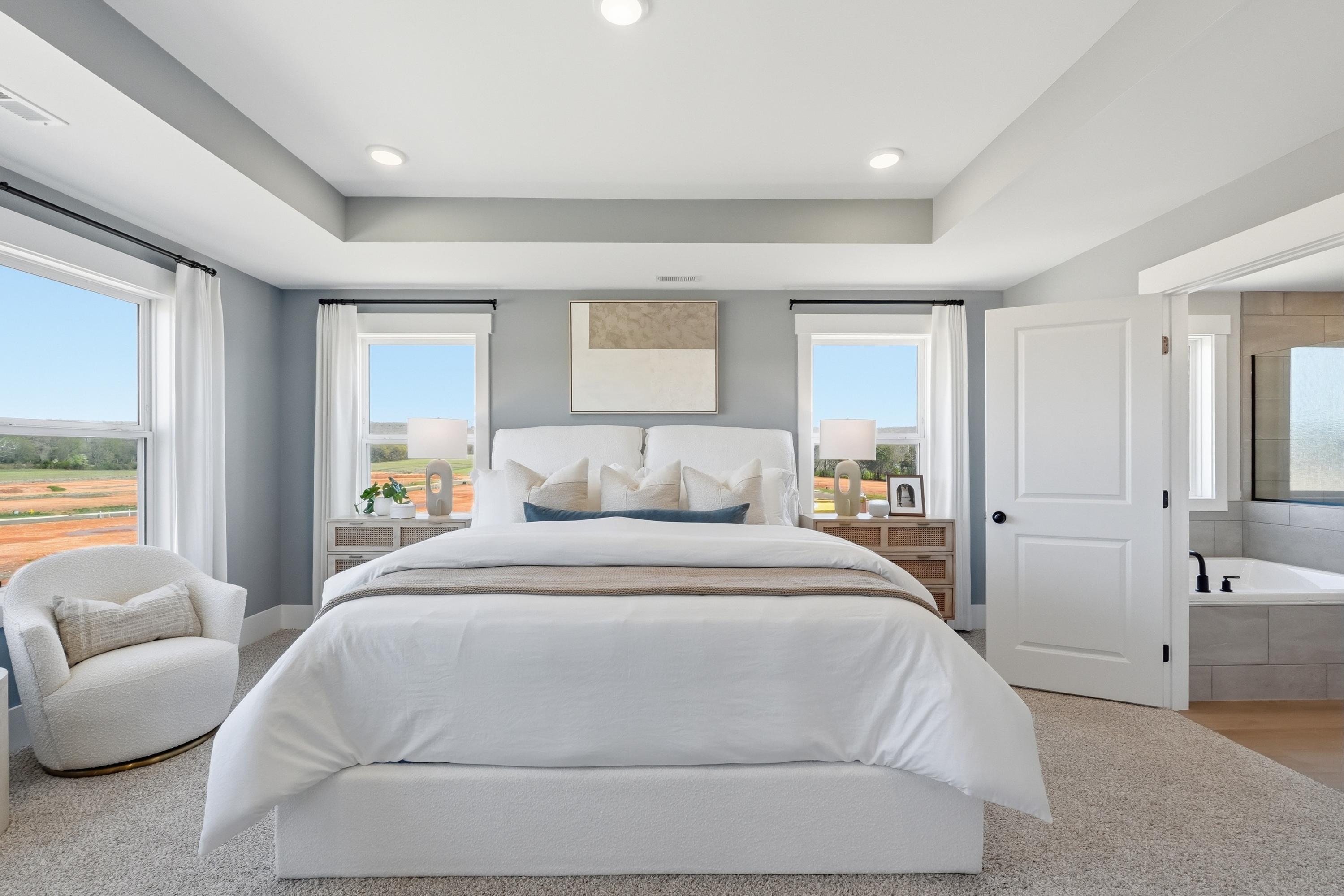 Modern primary bedroom in Berry Cove New Market AL with white king bed, gray walls, large windows, and en-suite tub bathroom