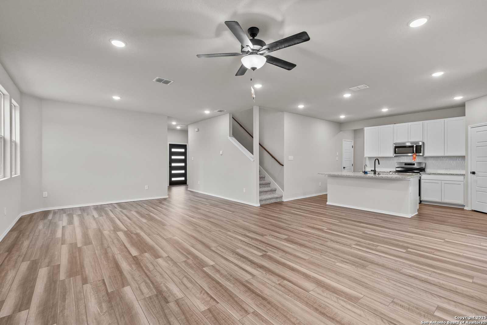 Open-concept living room and kitchen with white cabinets, island, luxury vinyl plank floors, and staircase in Davidson Homes The Murray I, San Antonio