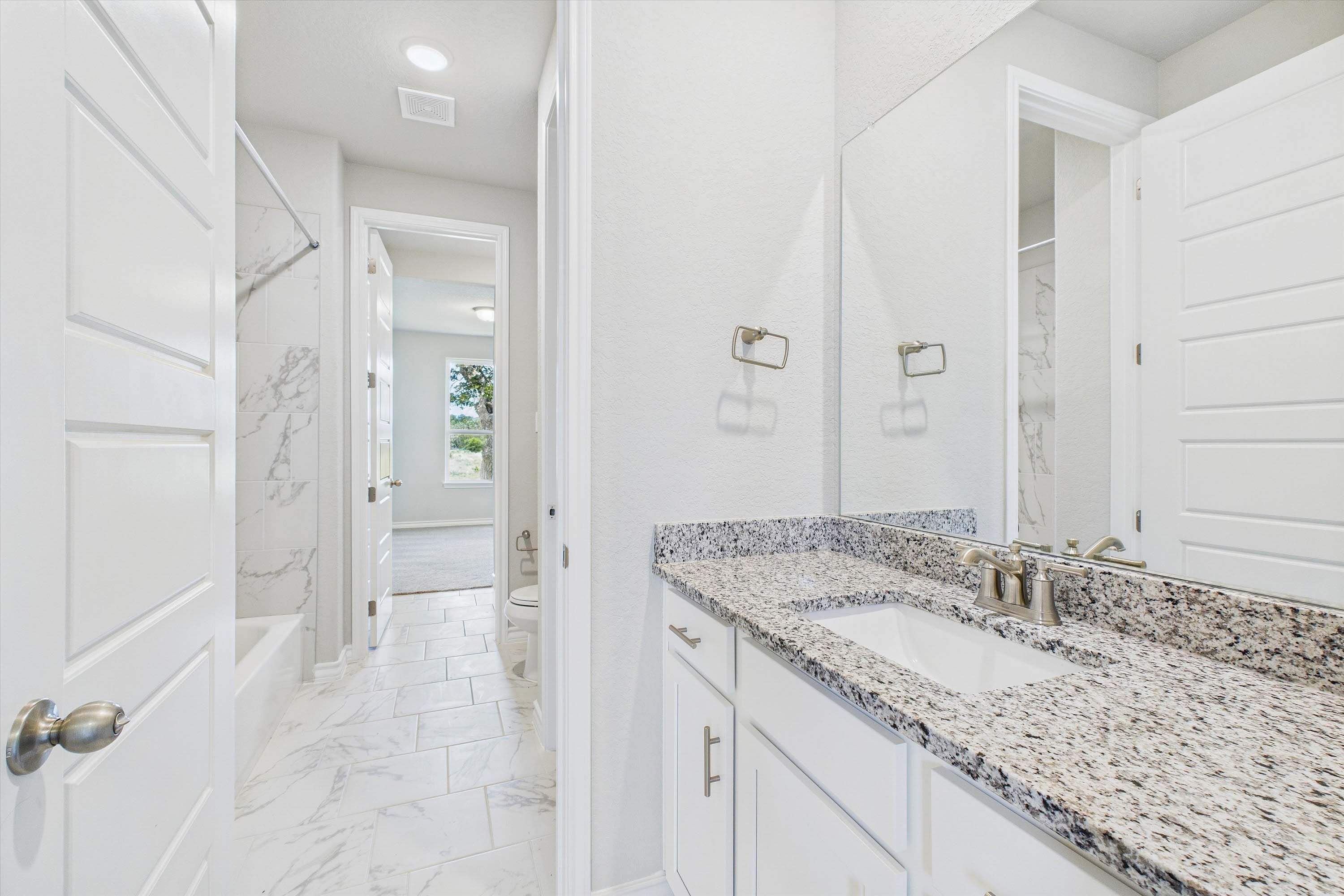 Modern bathroom in The Foster featuring a granite vanity, marble-style tile flooring, and a tub-shower combo.