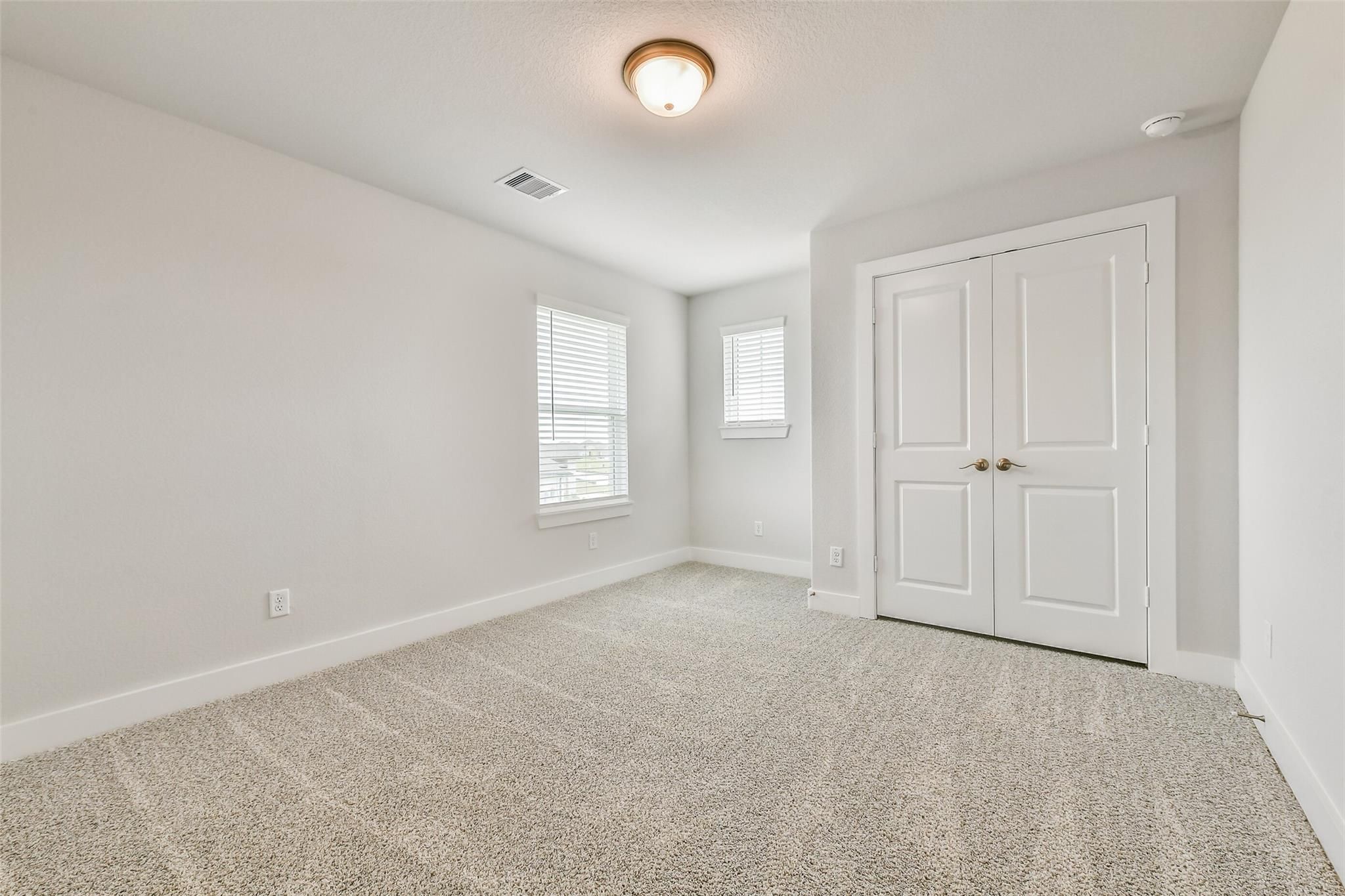 Bright secondary bedroom with light gray walls, beige carpet, double closet doors, and window blinds in Davidson Homes Victoria A, Lago Mar Texas