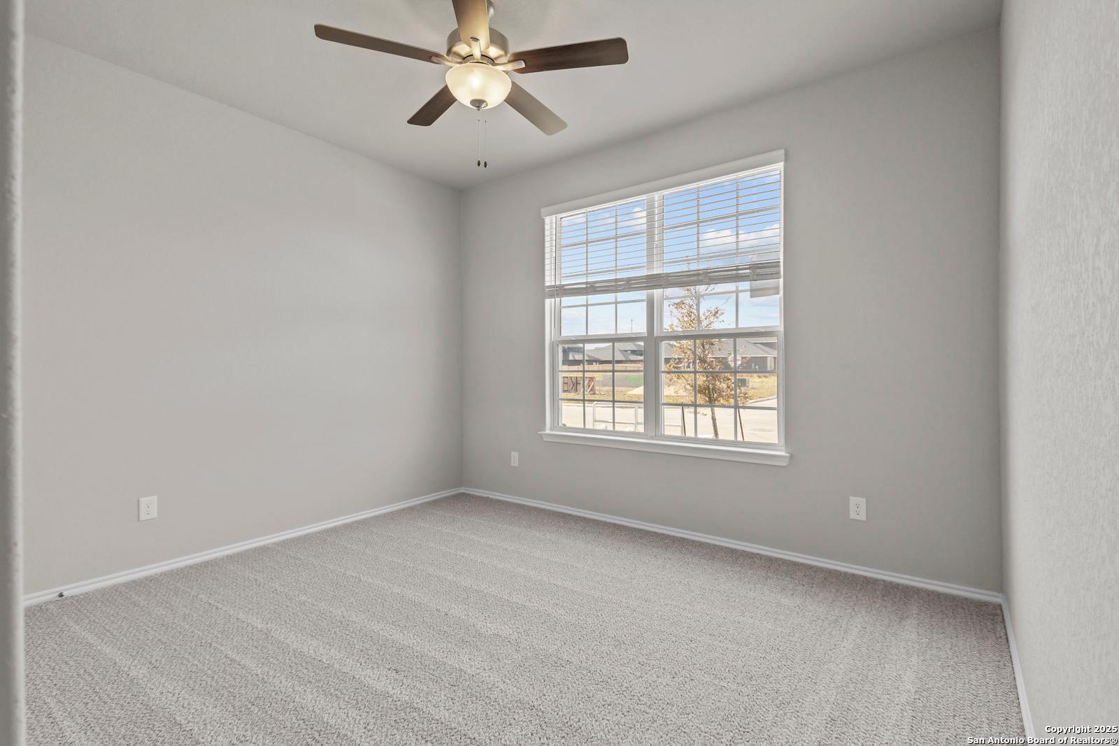 Bright secondary bedroom with ceiling fan, carpet flooring, and large window view in Davidson Homes The Collin B, Seguin, Texas