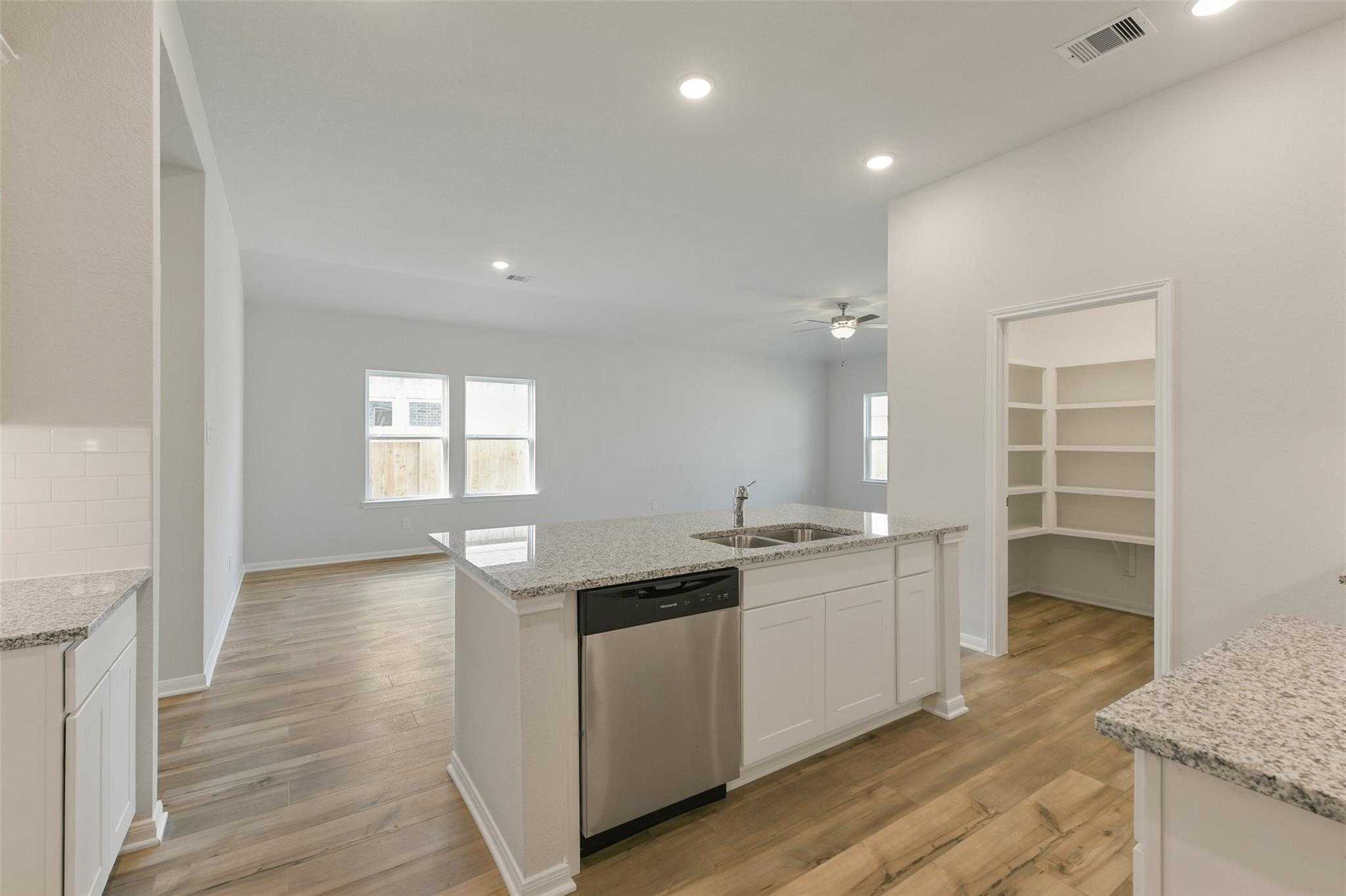 Modern open-concept kitchen with granite island, stainless sink, dishwasher, white cabinets, and hardwood floors in The Laguna B home, Dayton, Texas