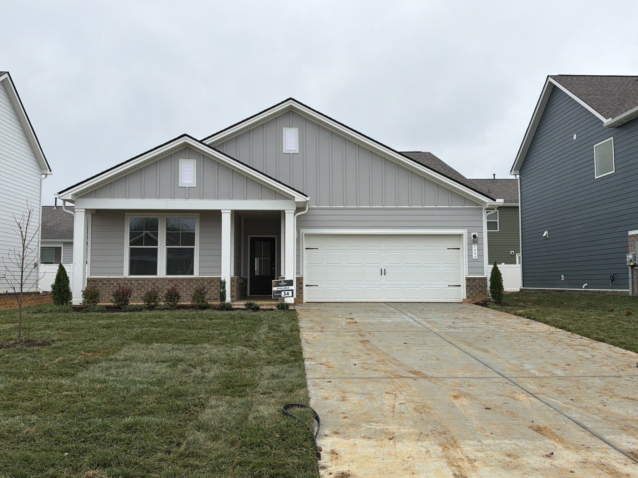 Modern gray single-story 3-bedroom home with 2-car garage, covered porch, and lush lawn in Sage Farms, White House, Tennessee