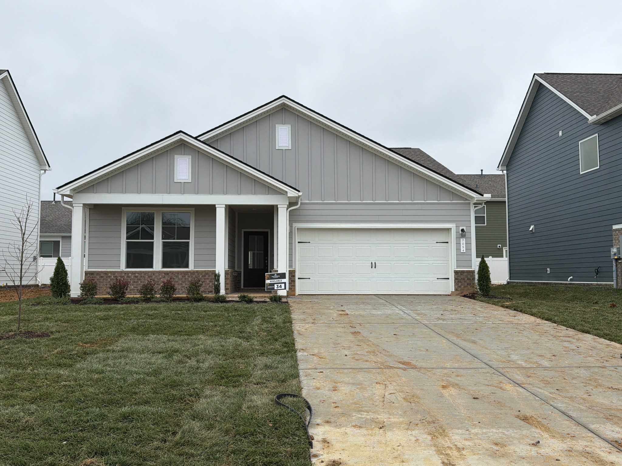Modern gray single-story 3-bedroom home with 2-car garage, covered porch, and lush lawn in Sage Farms, White House, Tennessee