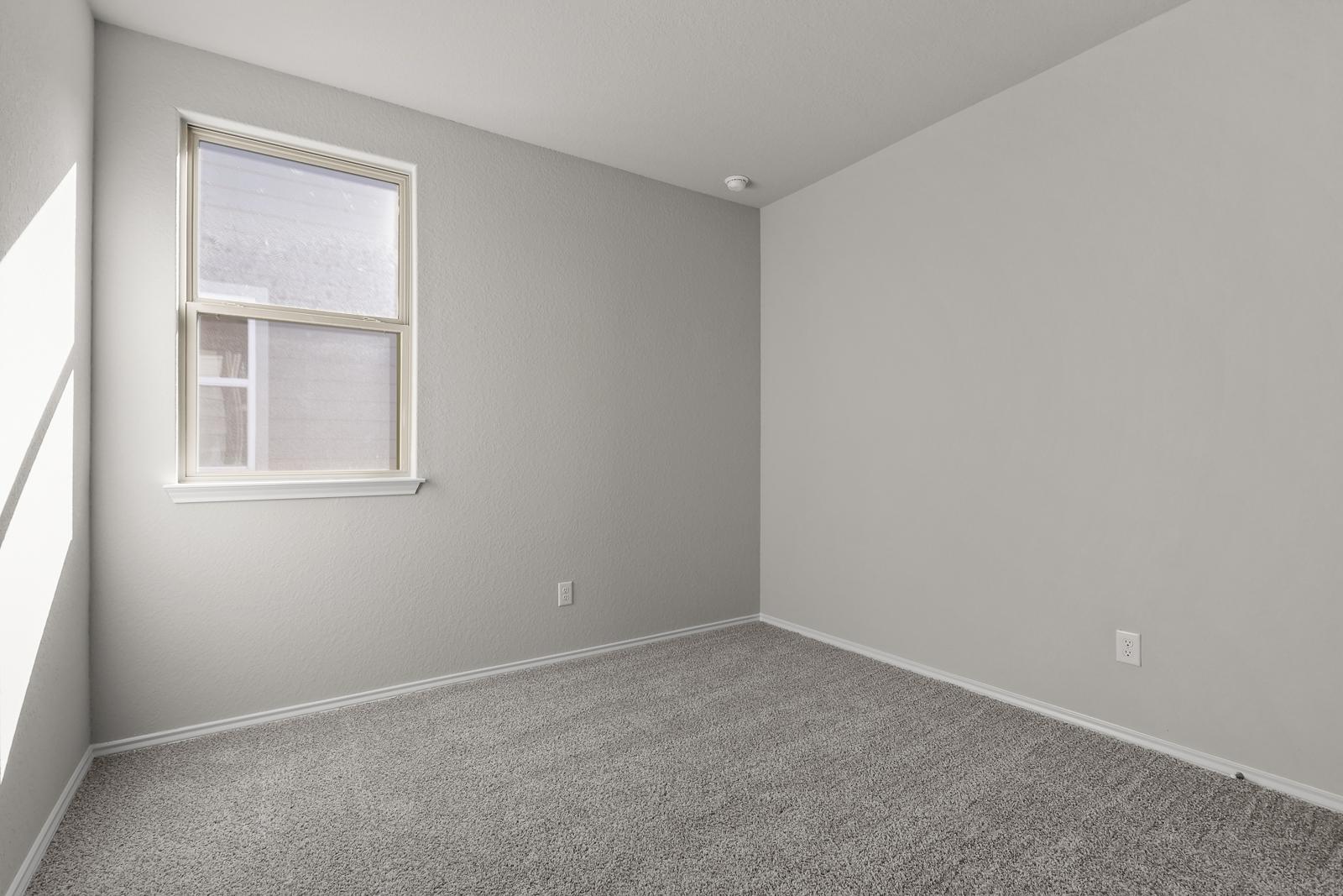 Bright, carpeted bedroom in The Arroyo home design by Davidson Homes, featuring neutral gray walls and natural light.