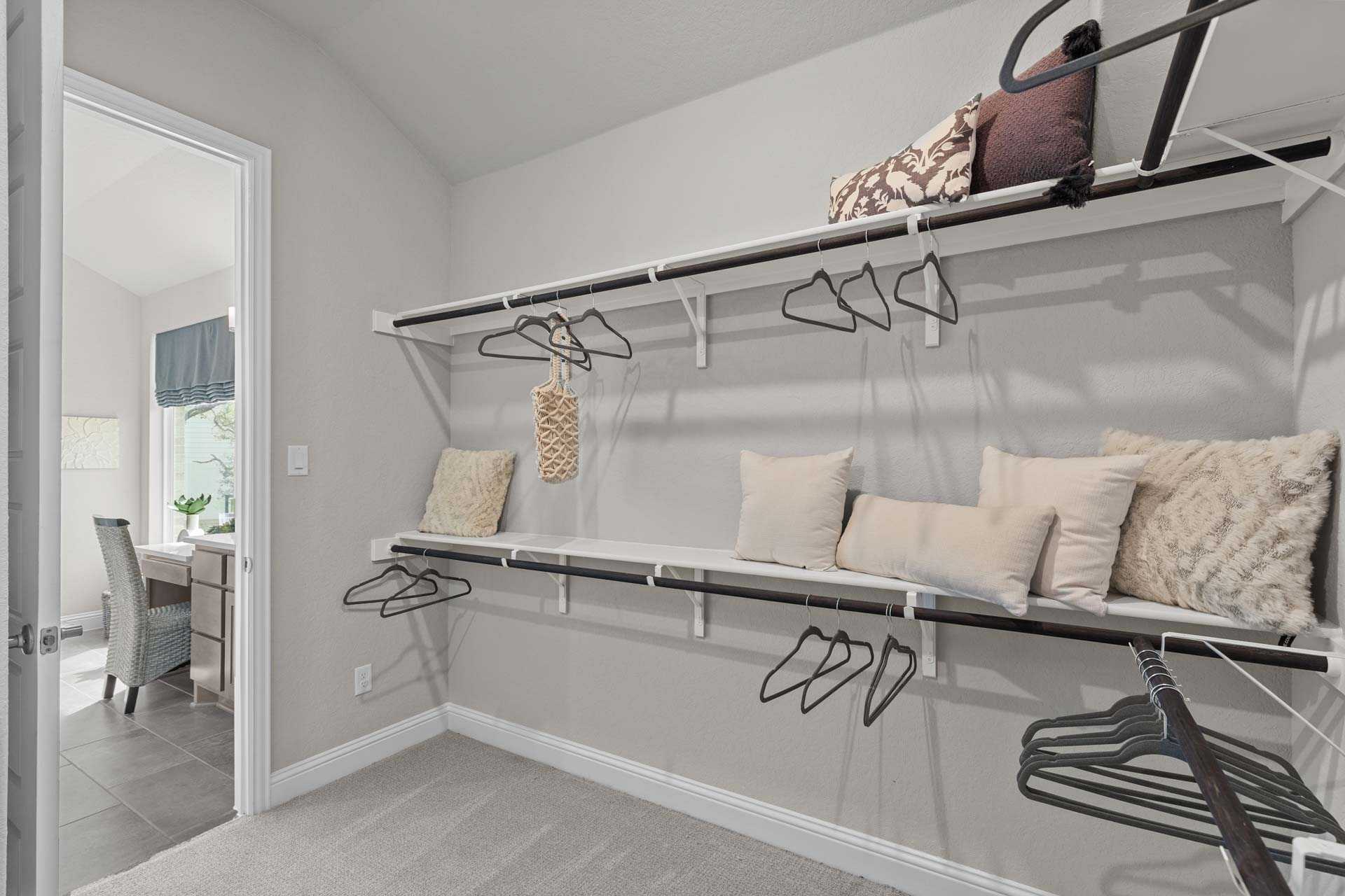 Spacious walk-in master closet in The Garner A with built-in shelves, hanging rods, pillows, and neutral gray tones